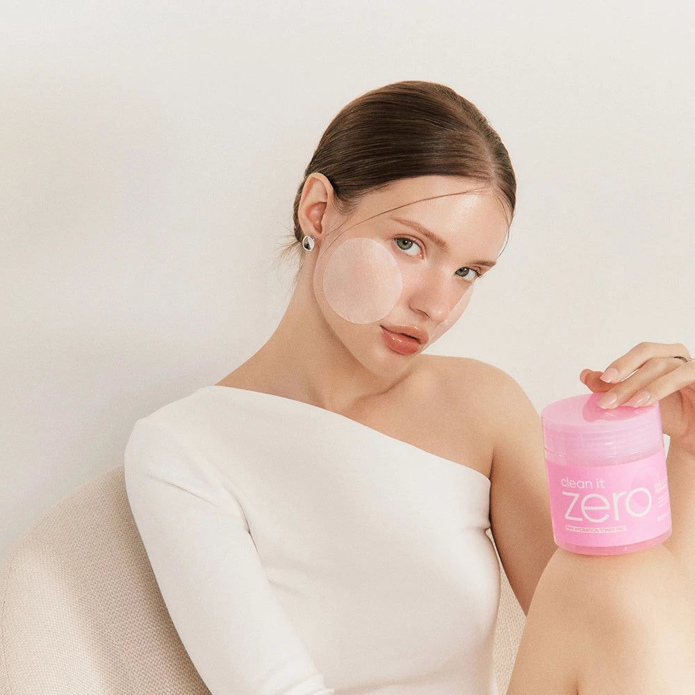 Una donna tiene un barattolo rosa con "Clean it Zero". Sul suo viso ci sono dei pad.