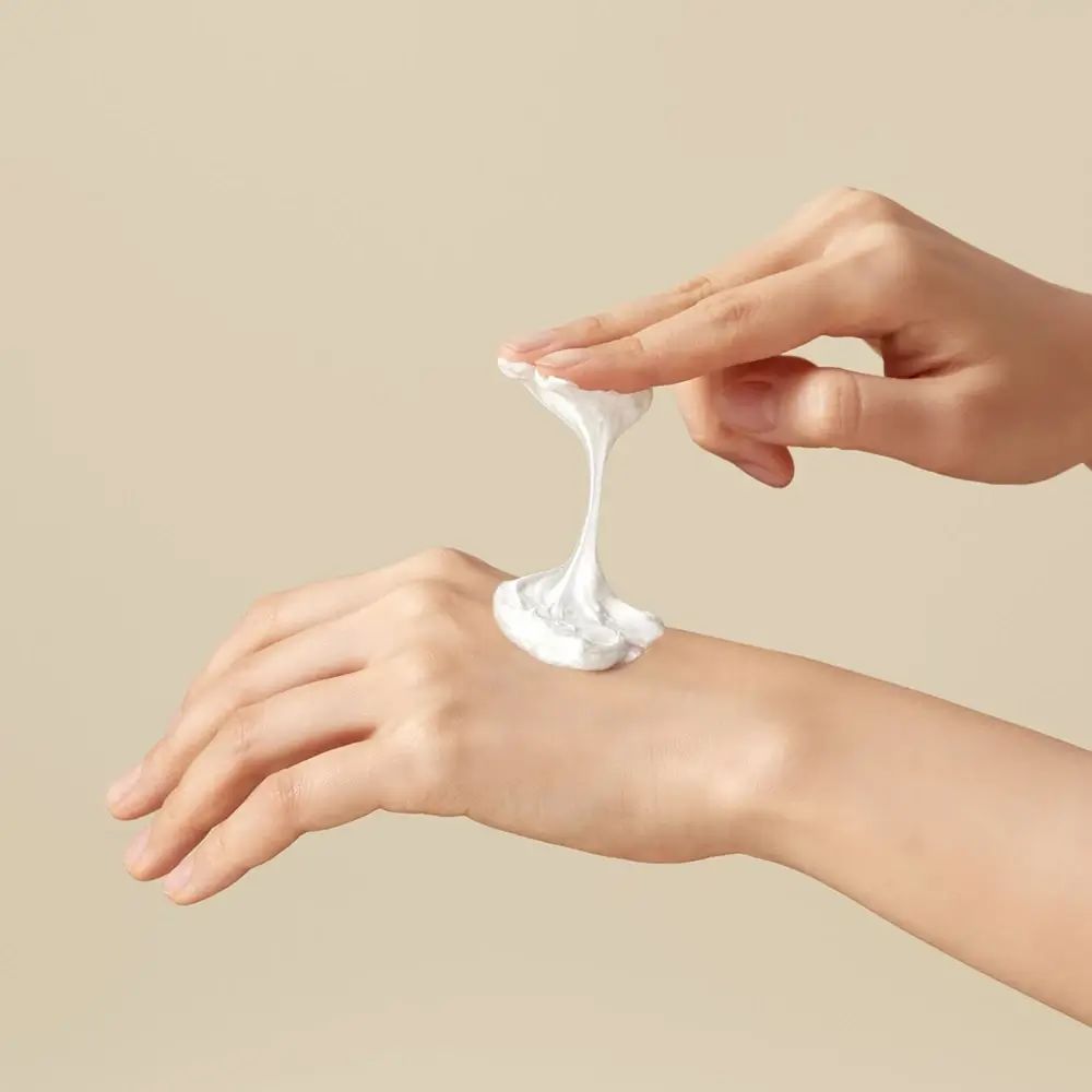 Mani con schiuma detergente bianca. La schiuma viene applicata sulla mano. Sfondo beige.