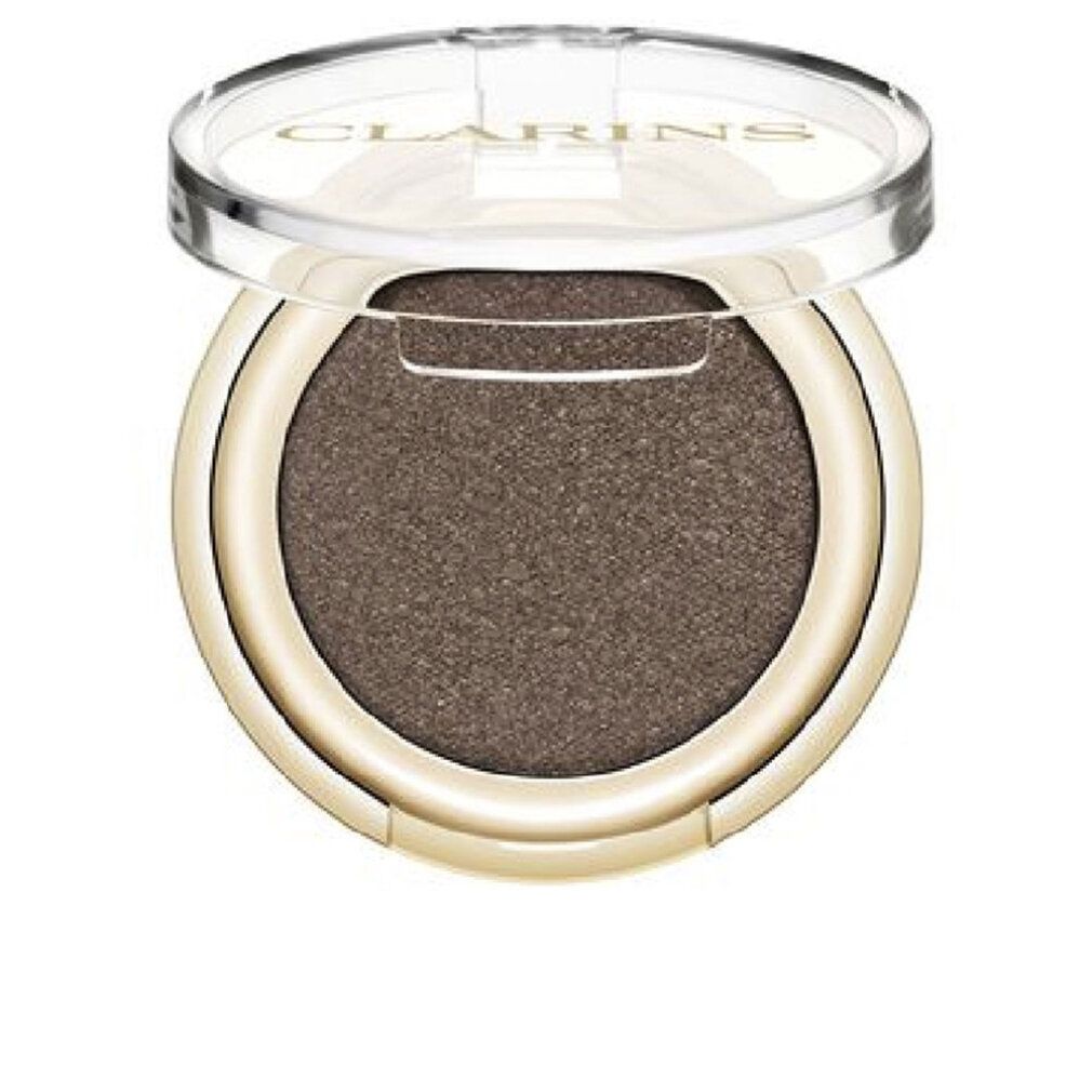 Contenitore rotondo dorato per ombretto con coperchio trasparente. L'ombretto è marrone. Il marchio Clarins è visibile sul coperchio.