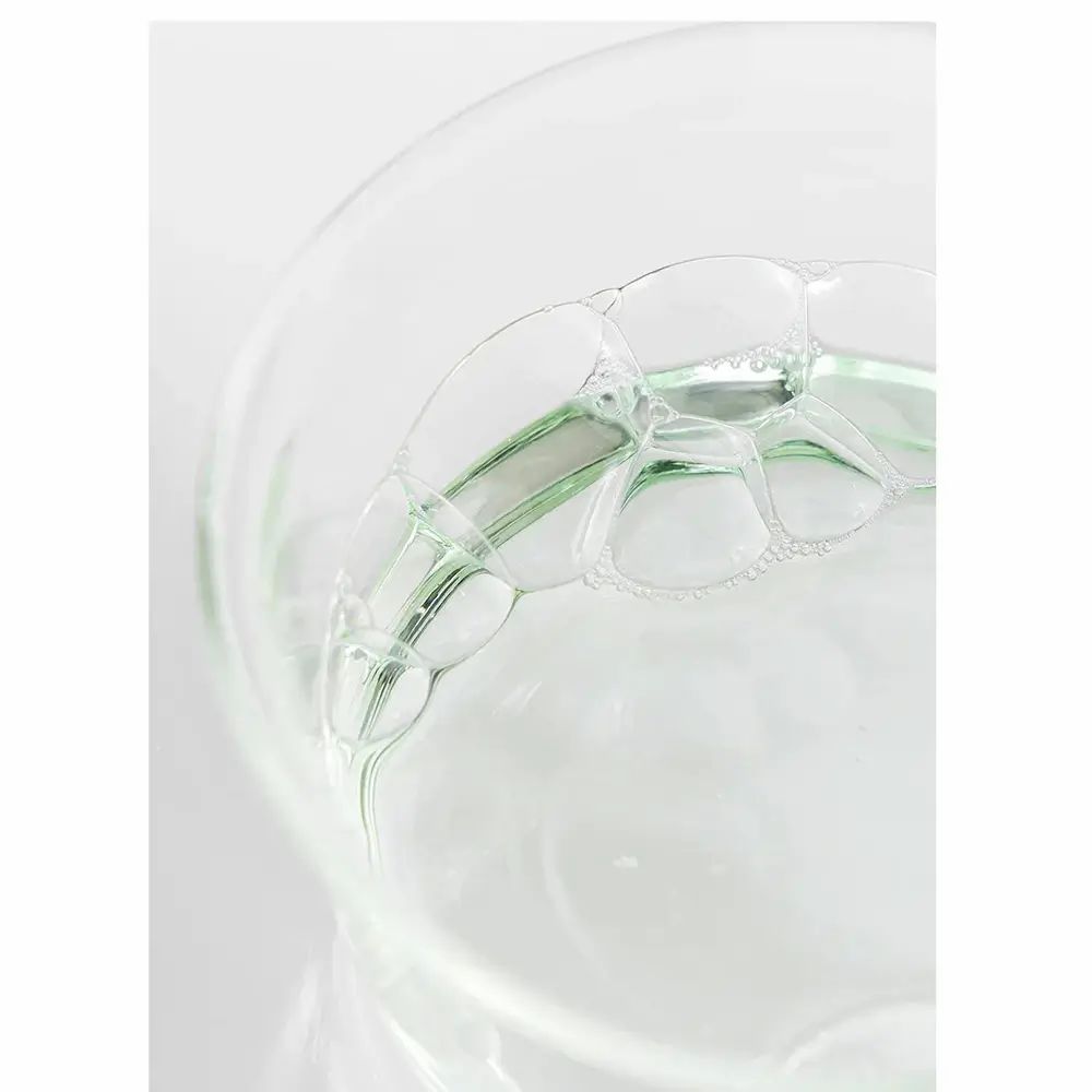Primo piano del toner in vetro. Liquido verde chiaro con bolle. Apertura del flacone visibile.