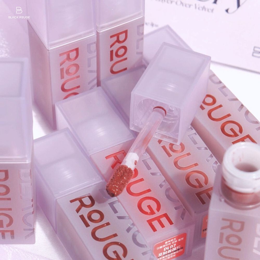 Diversi flaconi di lucidalabbra con tappi. Un flacone è aperto, l'applicatore è visibile. Sui flaconi c'è scritto « ROUGE ».