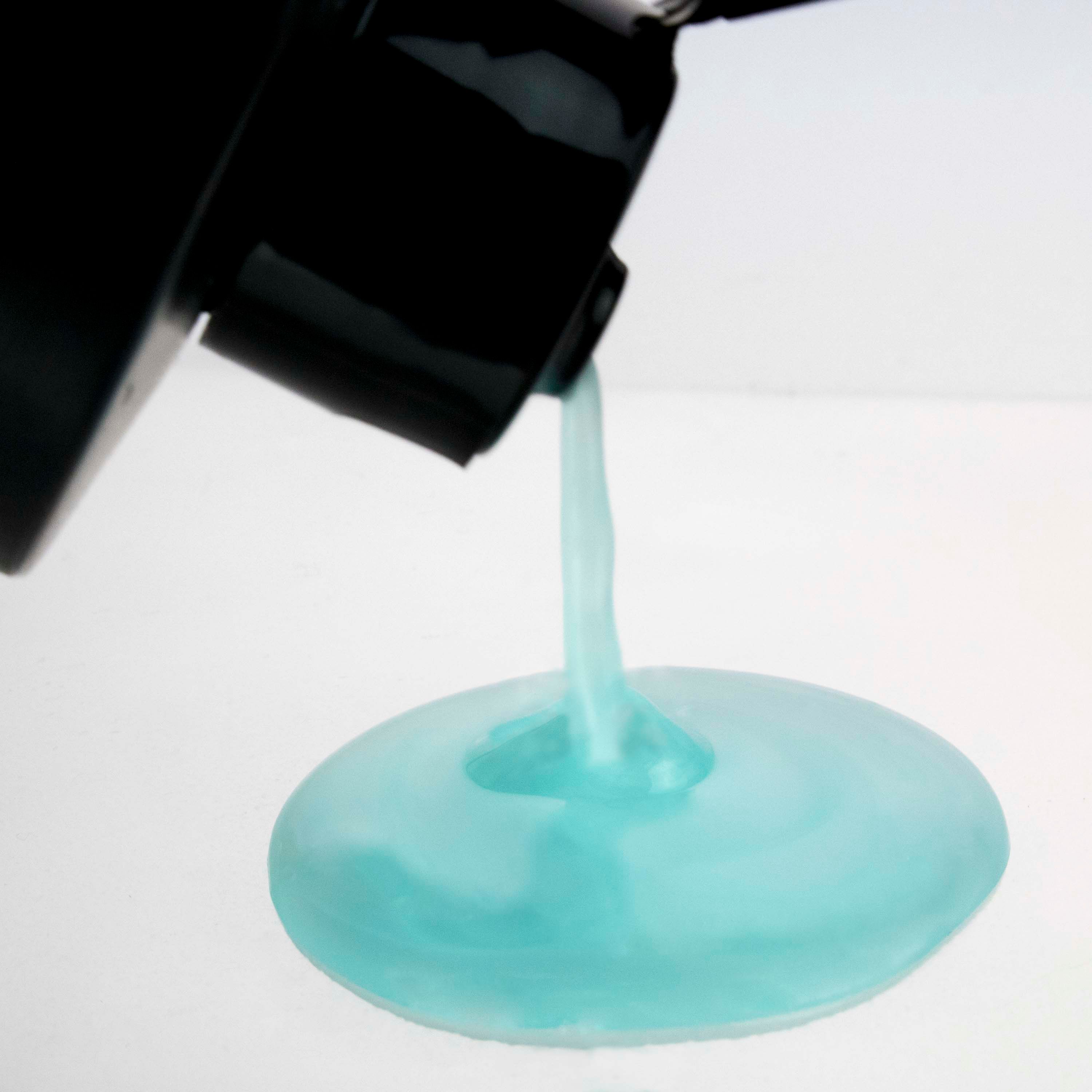 Dalla bottiglia nera esce shampoo blu su una superficie bianca.
