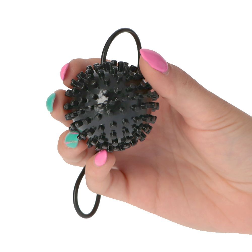 Sfera nera con borchie tenuta in una mano. La mano tiene il prodotto. Le unghie sono dipinte con smalto rosa e turchese.