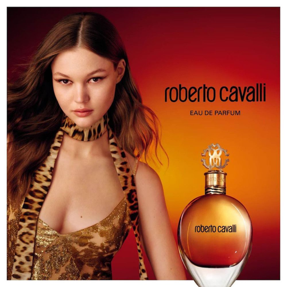 Flacone di profumo con tappo dorato e scritta. Donna con accessori leopardati. Sfondo rosso e arancione.