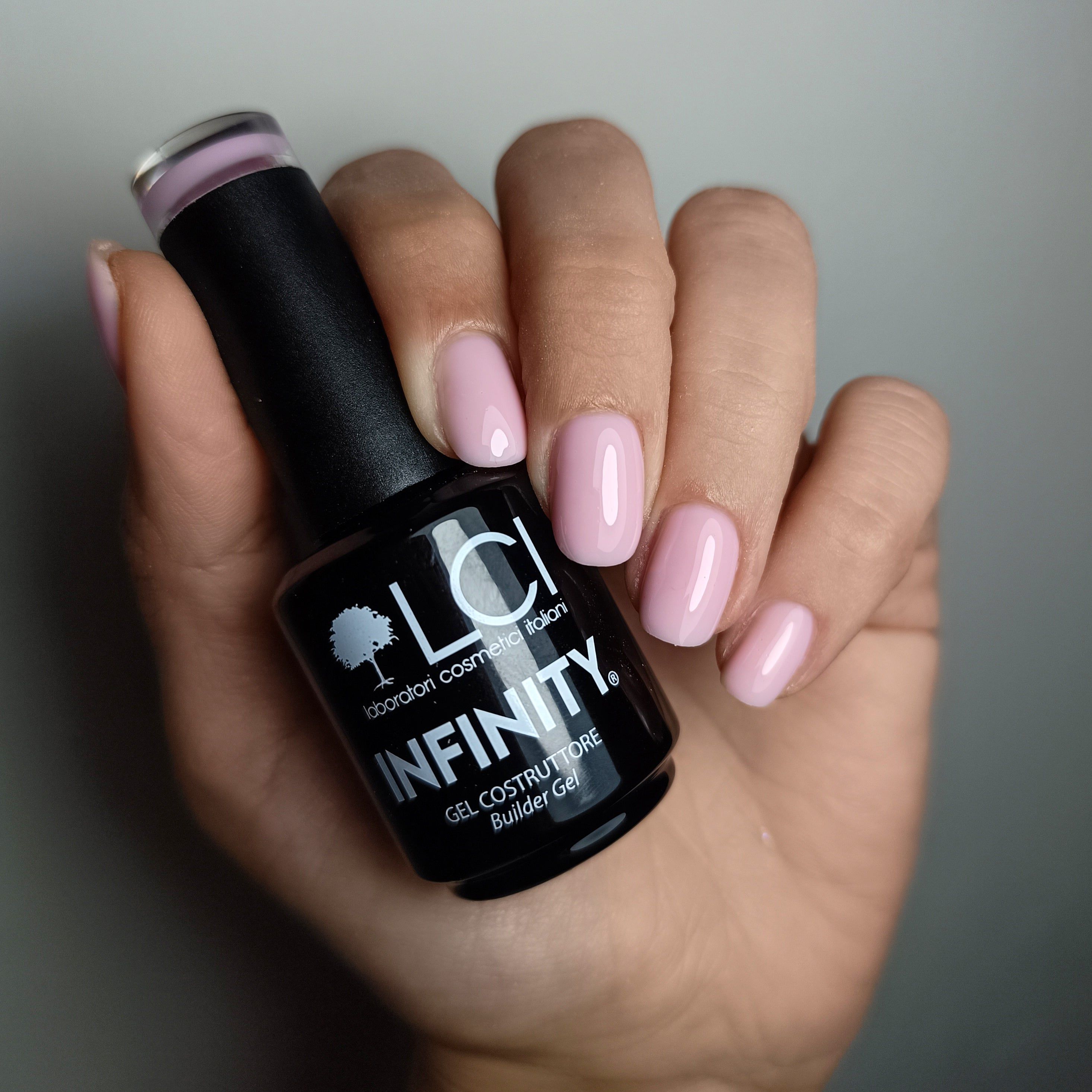 Mano con unghie smaltate di rosa. Flacone nero con scritta LCI INFINITY Builder Gel.