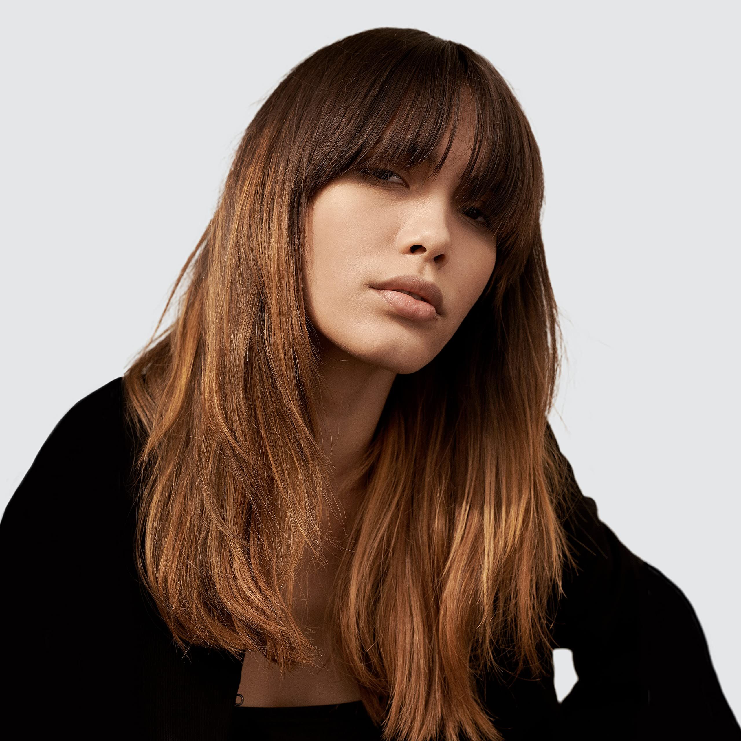 Ritratto di una donna con capelli castani e frangia. Guarda la fotocamera.