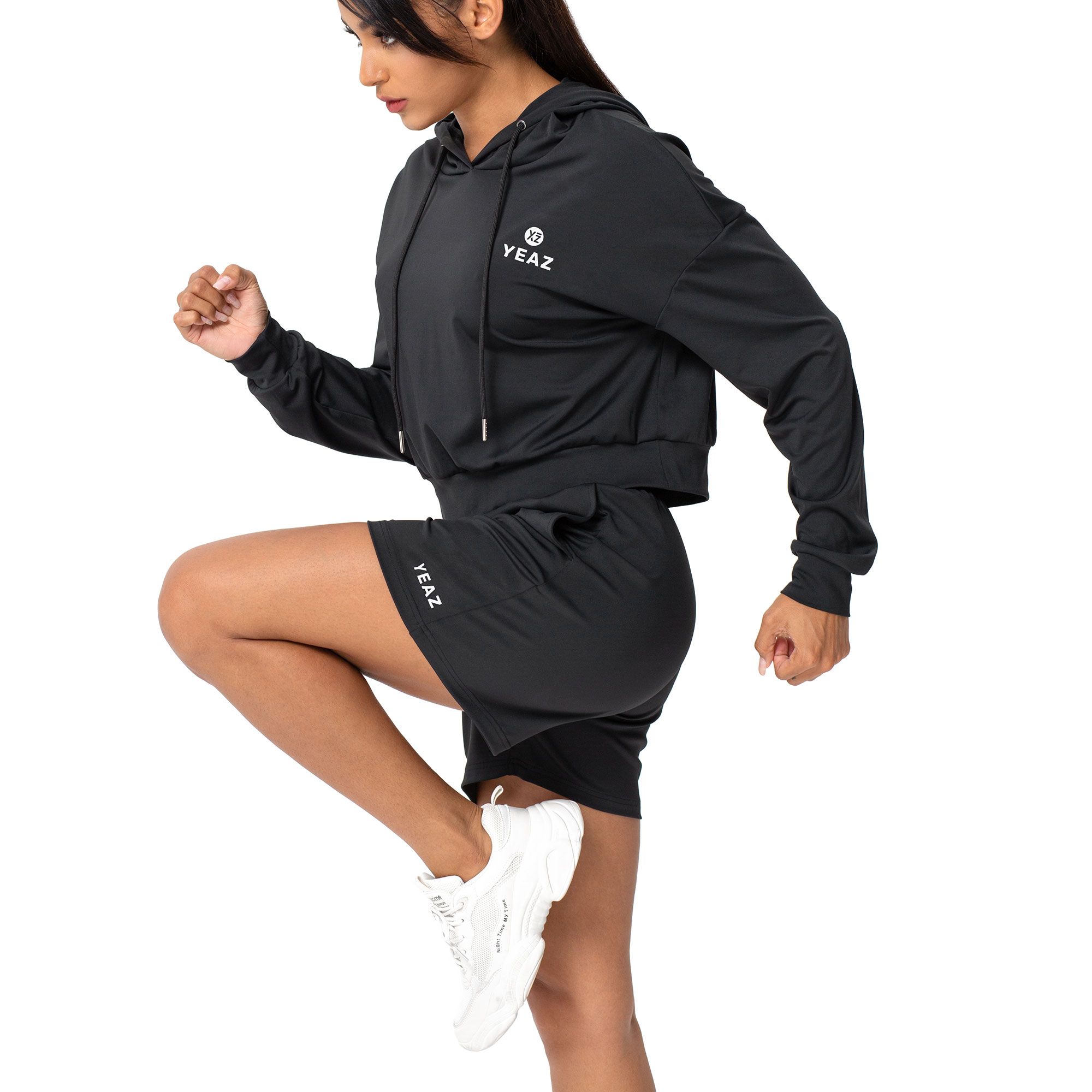 Donna con felpa corta nera e pantaloncini con logo 'YEAZ'.