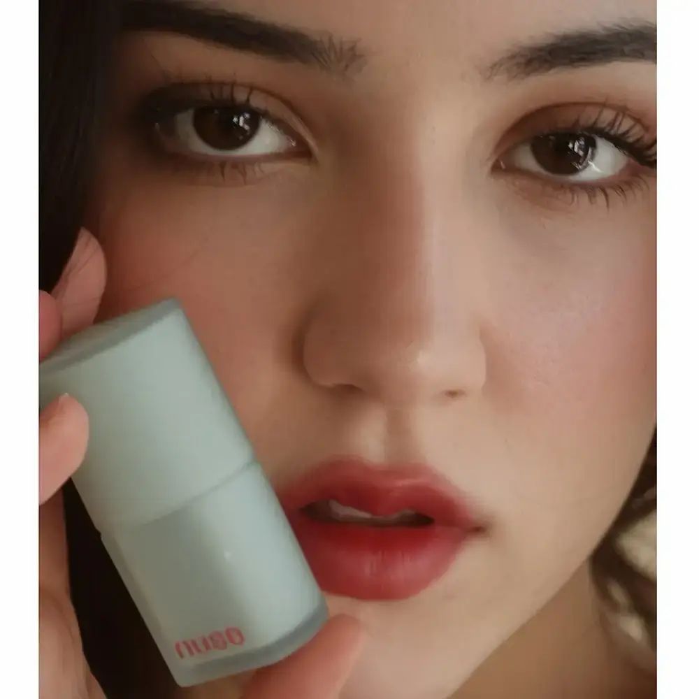 Donna che tiene un confezione di rossetto. Le labbra sono dipinte con il rossetto. Il rossetto è rosso.