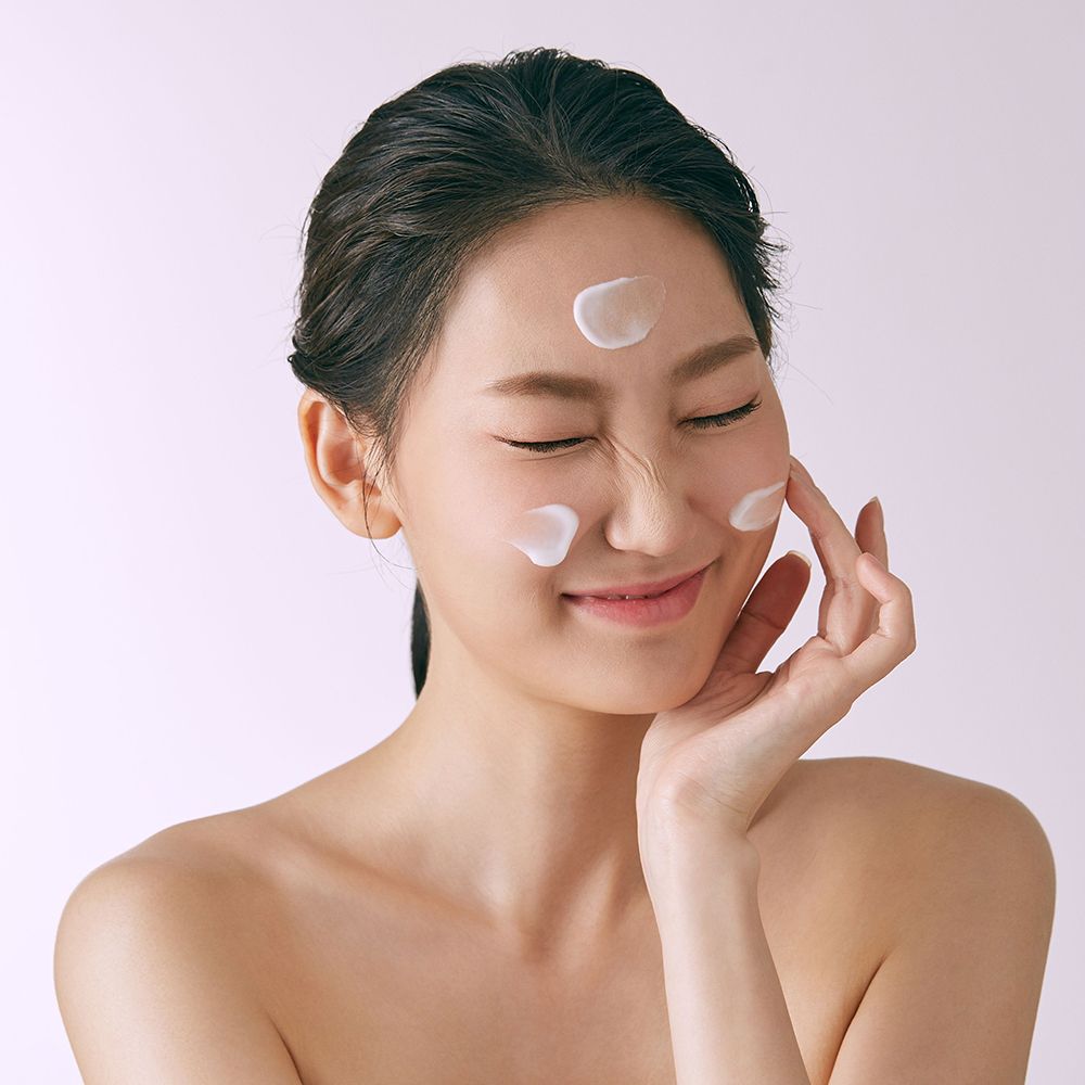 Donna con occhi chiusi, crema sulla pelle. Mani che toccano il viso.