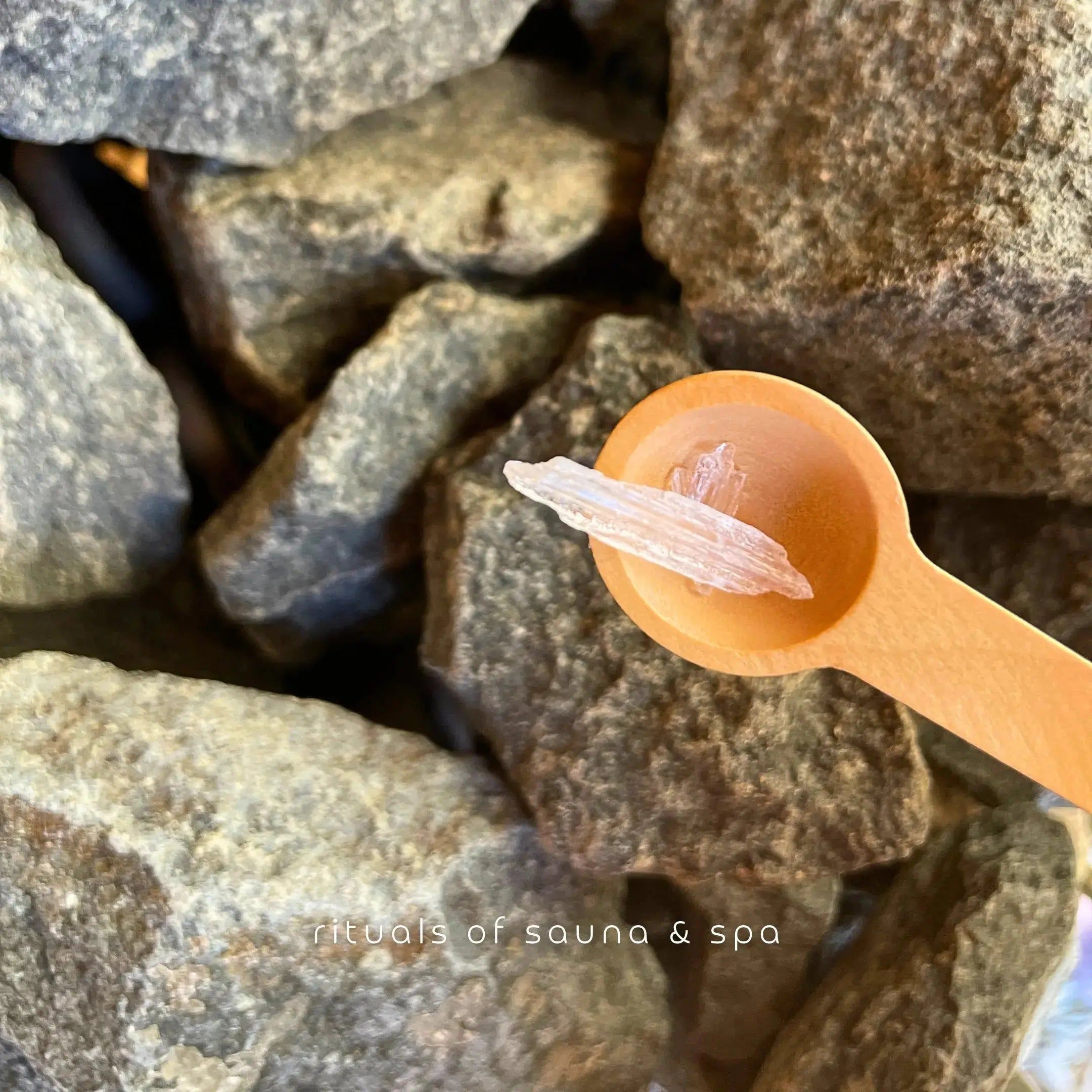 Cucchiaio di legno con cristalli di mentolo su pietre. Sfondo: pietre della sauna.