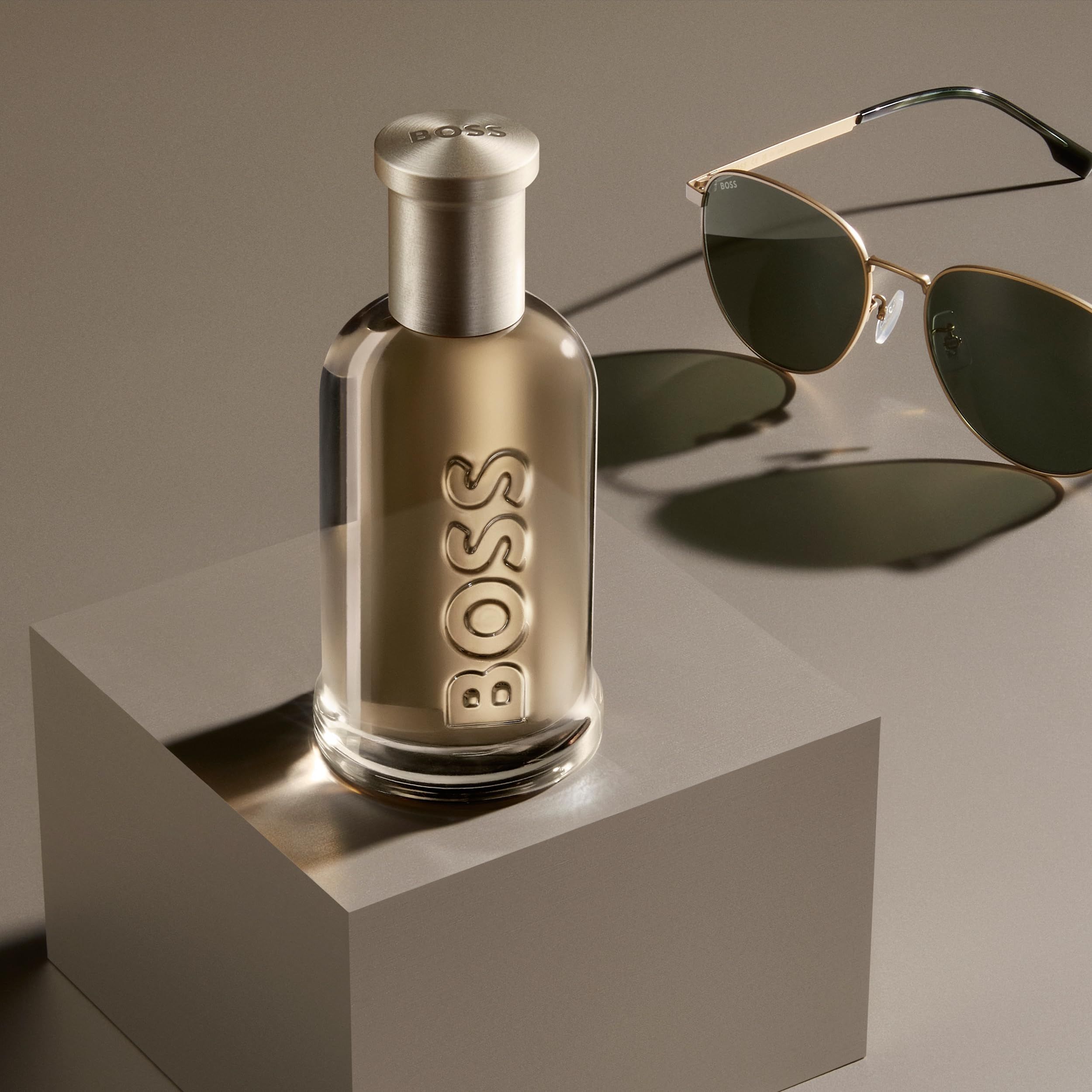 Flacone Hugo Boss Bottled Eau de Parfum su un cubo, accanto a occhiali da sole.