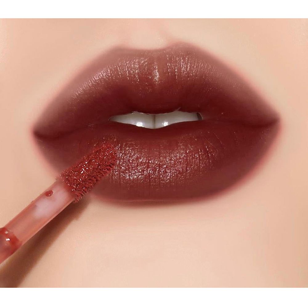 Primo piano di labbra coperte di lucidalabbra. L'applicatore è visibile. Colore scuro e lucido.
