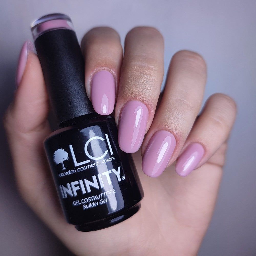 Mano che tiene un flacone di smalto gel e unghie smaltate. Flacone nero con scritta LCI INFINITY. Unghie smaltate rosa pastello.
