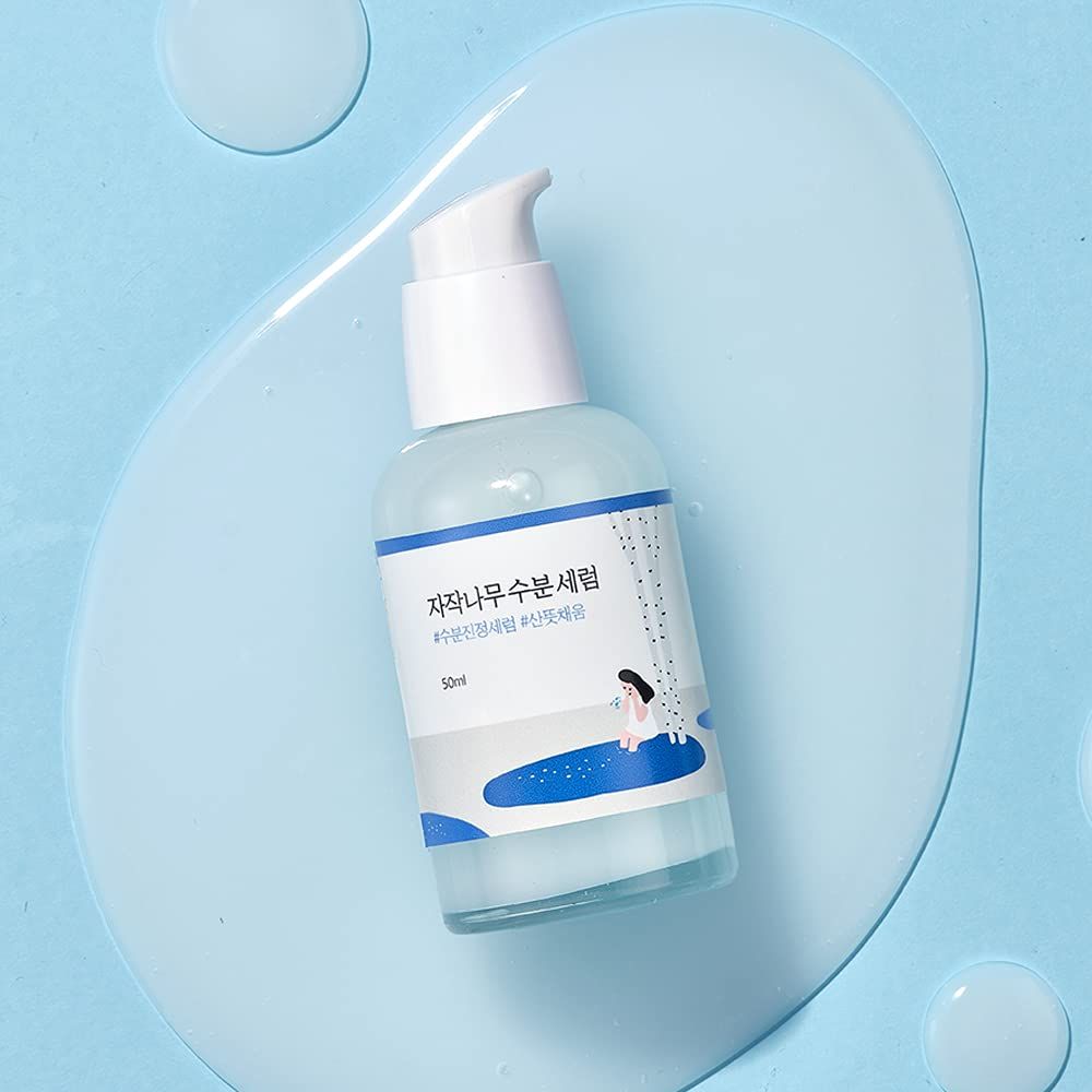 Flacone trasparente con dosatore bianco. Etichetta con caratteri e illustrazione. Appoggiato su liquido blu.