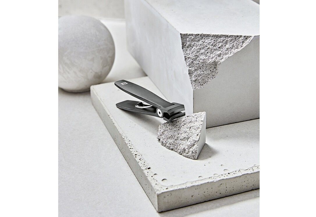 Tagliaunghie nero su una superficie di cemento. Logo ZWILLING visibile. Aperto, accanto a un blocco di cemento.