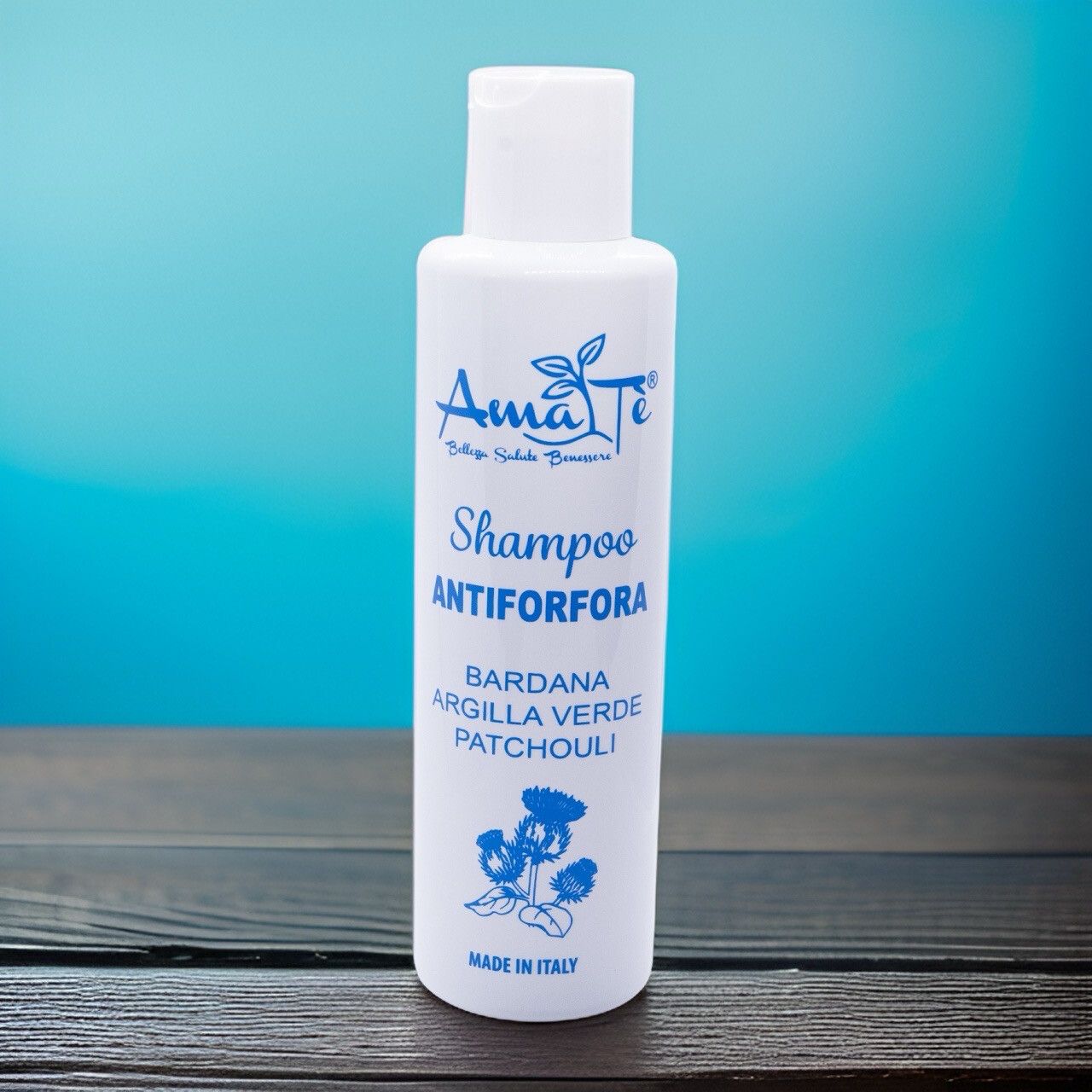 Flacone bianco con etichetta blu. Testo: Shampoo Antiforfora, ingredienti. Su superficie in legno.