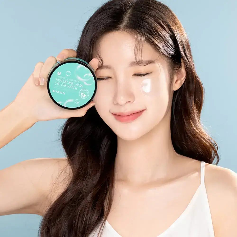 Donna tiene un barattolo di patch per occhi. Un patch è visibile sulla pelle. Il barattolo indica "Hyaluronic Acid Eye Gel Patch".