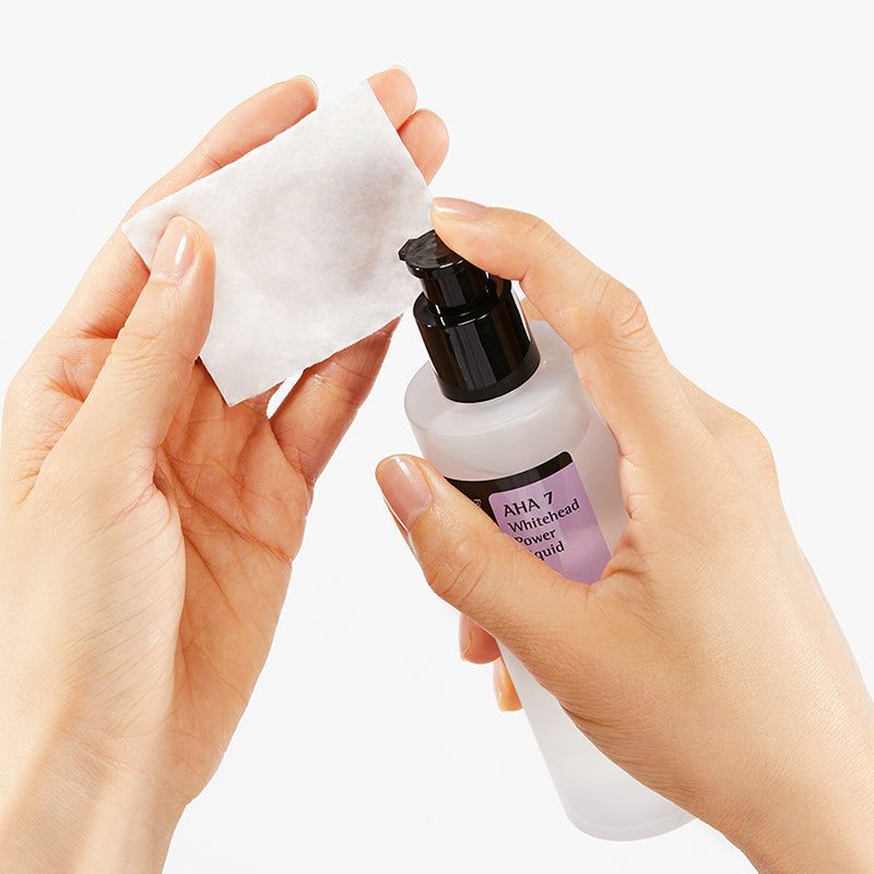 Mani che tengono un batuffolo di cotone e un flacone. AHA 7 Whitehead Power Liquid. Marchio: COSRX.