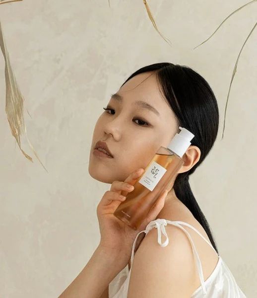 Una donna tiene una bottiglia di Beauty of Joseon Revive Serum vicino alla guancia.
