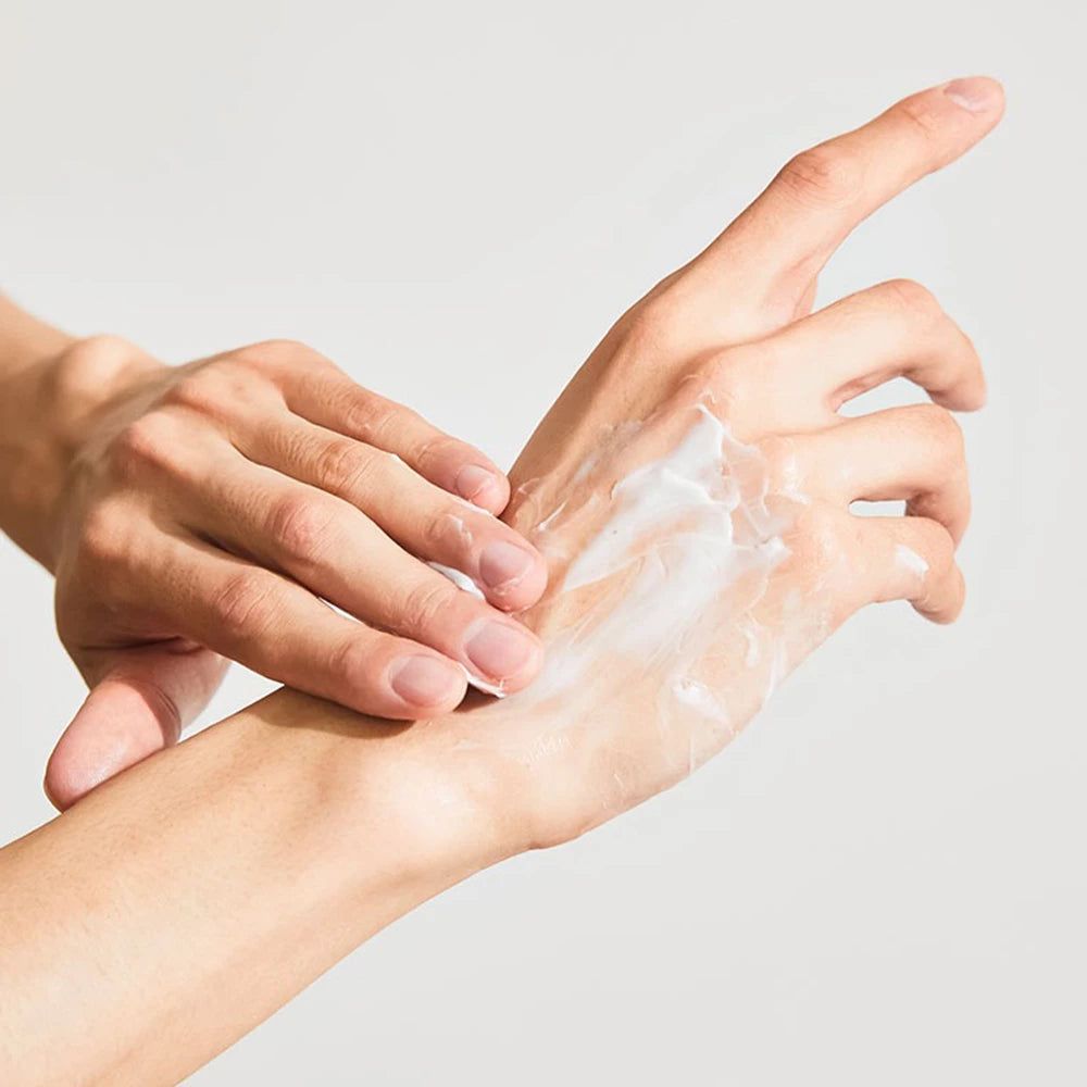 Mani che applicano crema sulla pelle. Crema bianca sulla mano. Sfondo chiaro.