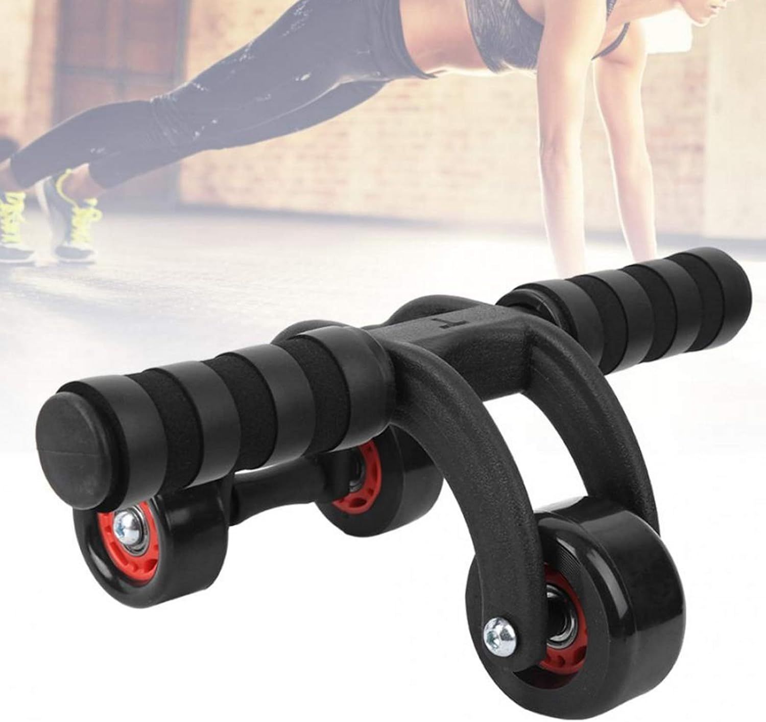 Ruota fitness con tre ruote e maniglie. Design nero con dettagli rossi. Persona sullo sfondo che si allena.