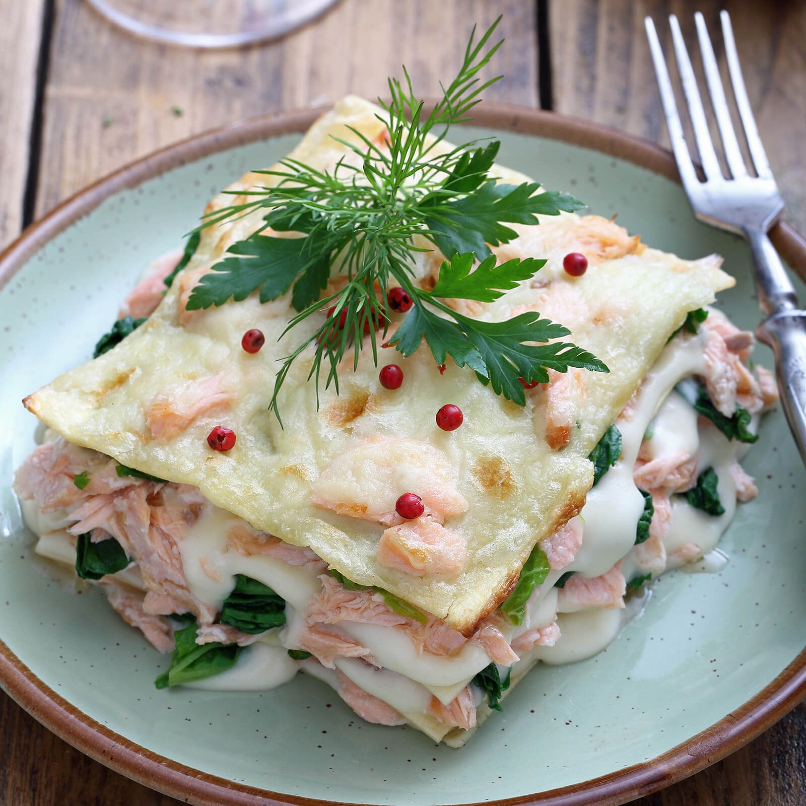 Lasagne su un piatto verde. Strati di pasta, salmone, spinaci e formaggio. Guarnite con erbe.