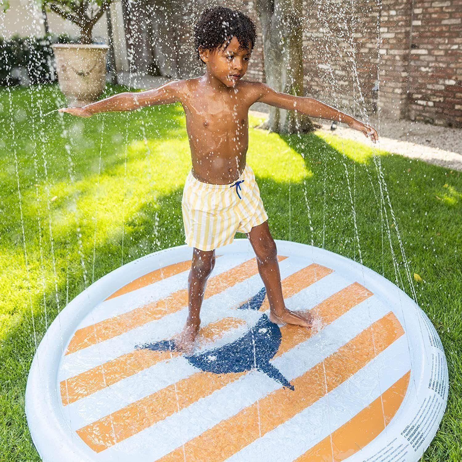 Bambino in pantaloncini a righe gialle su tappeto rotondo con motivo squalo e spruzzi d'acqua.