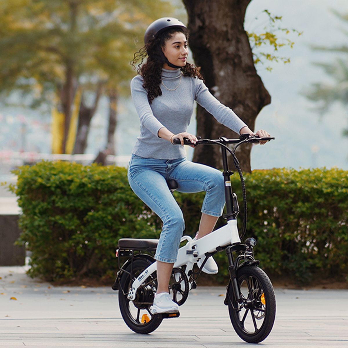 Persona che guida una e-bike bianca. La persona indossa un casco e jeans.