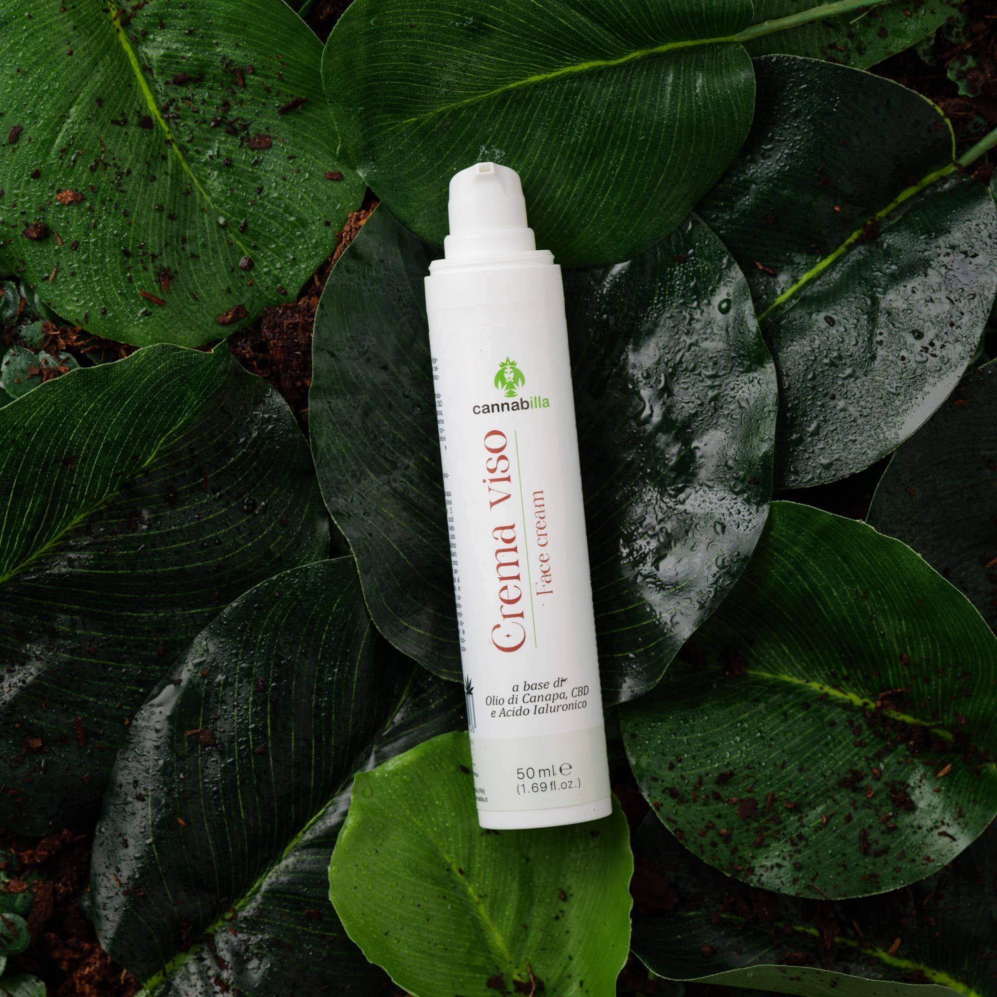 Flacone bianco di crema viso Cannabilla su foglie. Testo: Crema viso, face cream. Logo e scritta Cannabilla. 50 ml.