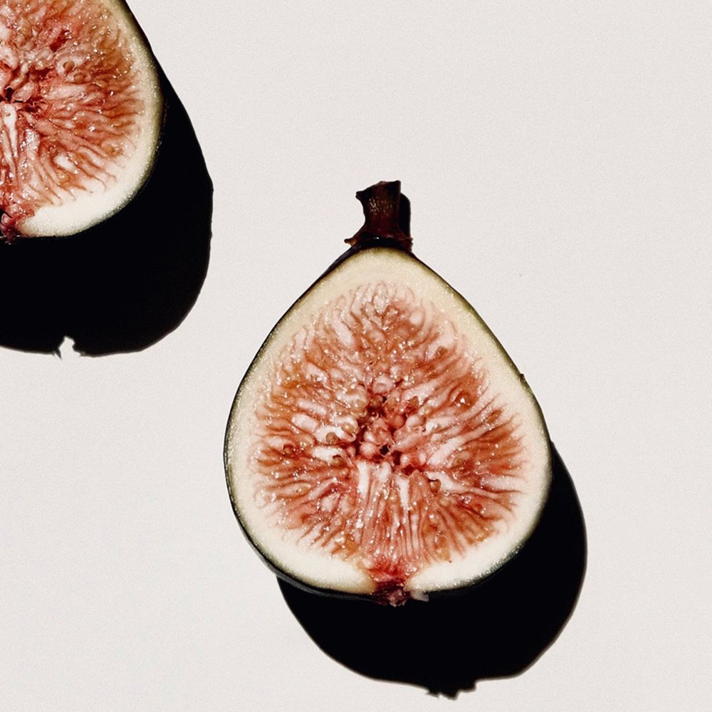 Due fichi a metà su sfondo bianco. Polpa rosa, buccia verde-viola. Ombra.