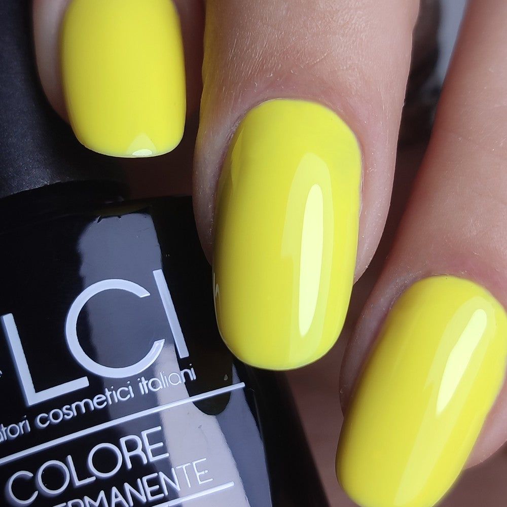Smalto giallo sulle unghie. Flacone LCI sullo sfondo.