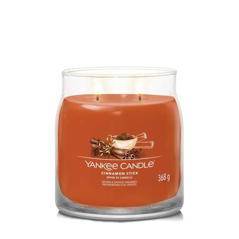 Vaso di vetro con cera arancione. Scritta: Yankee Candle, Cinnamon Stick, 368 g. Illustrazione di bastoncini di cannella.