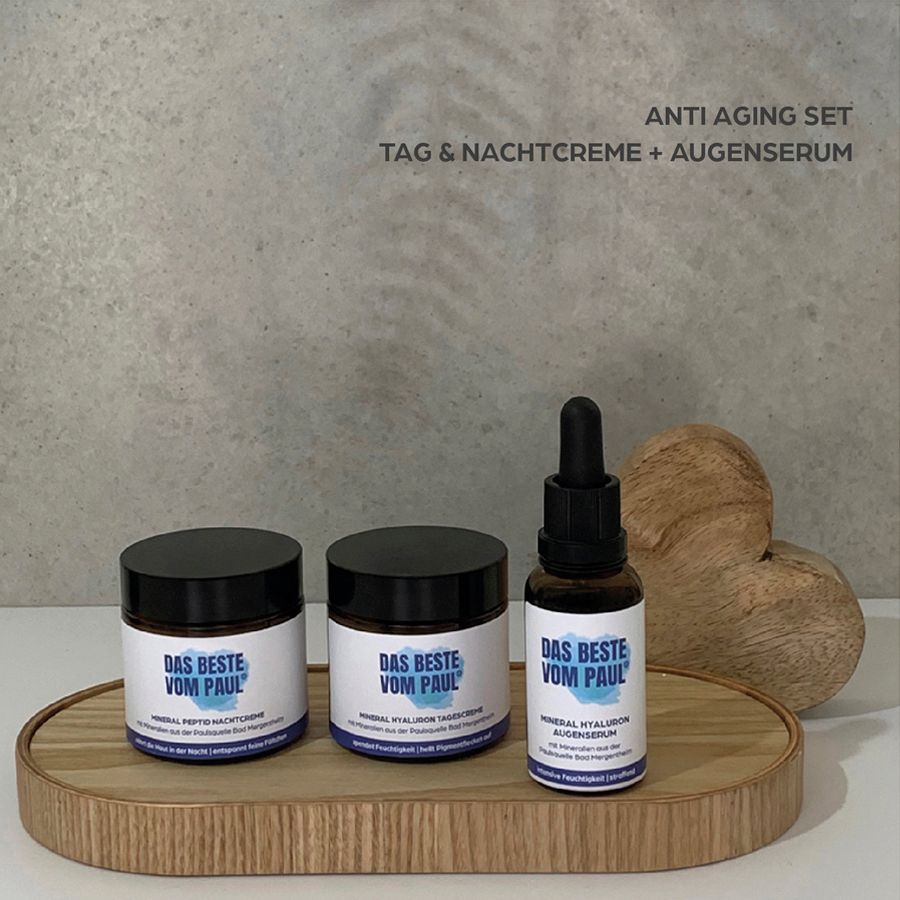 Tre prodotti su un vassoio di legno: crema giorno, crema notte e siero occhi. Testo: ANTI AGING SET.