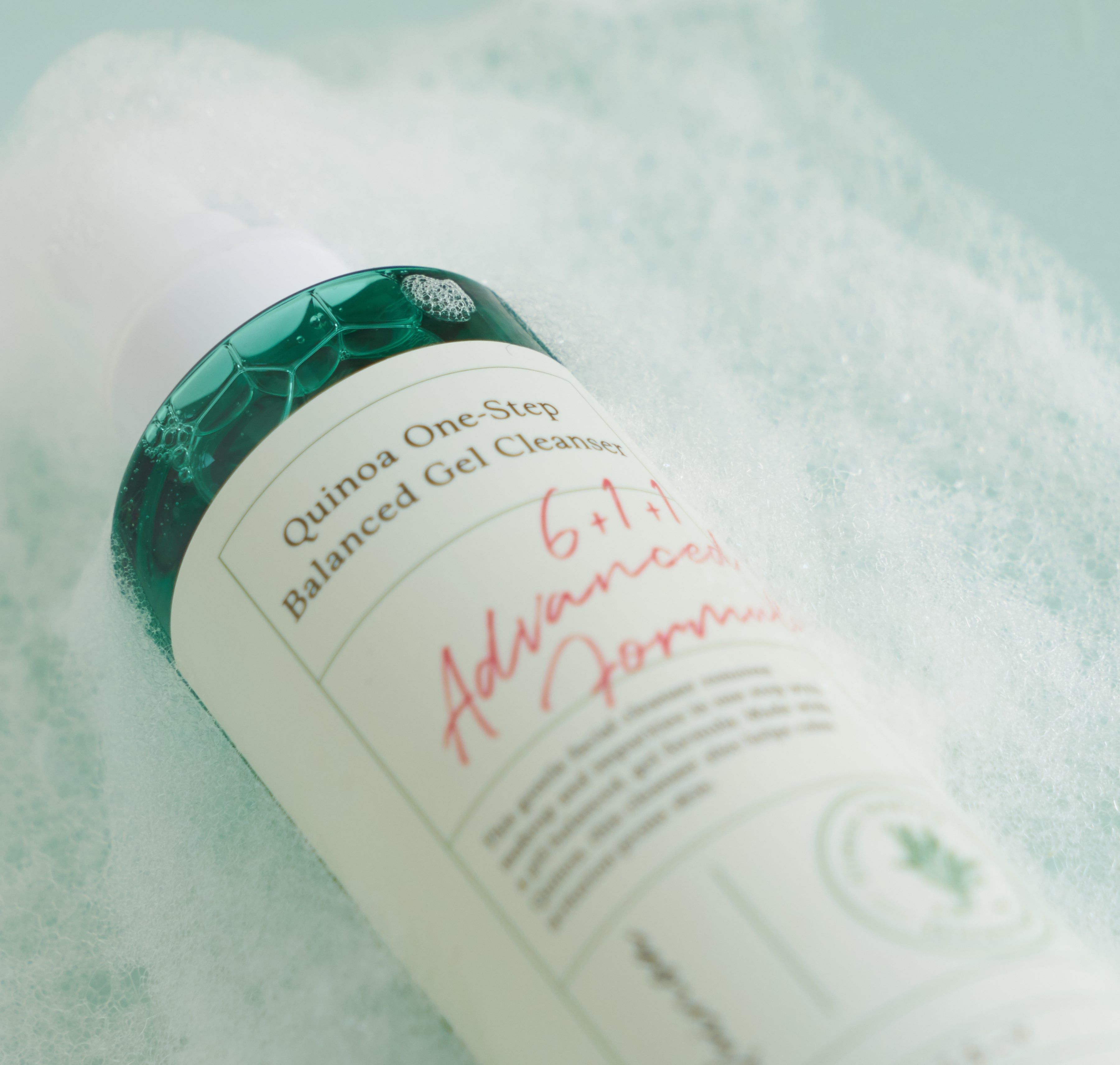 Primo piano del flacone in bolle di sapone. Scritta: Quinoa One-Step Balanced Gel Cleanser, 6+1+1 Advanced Formula. Schiuma.