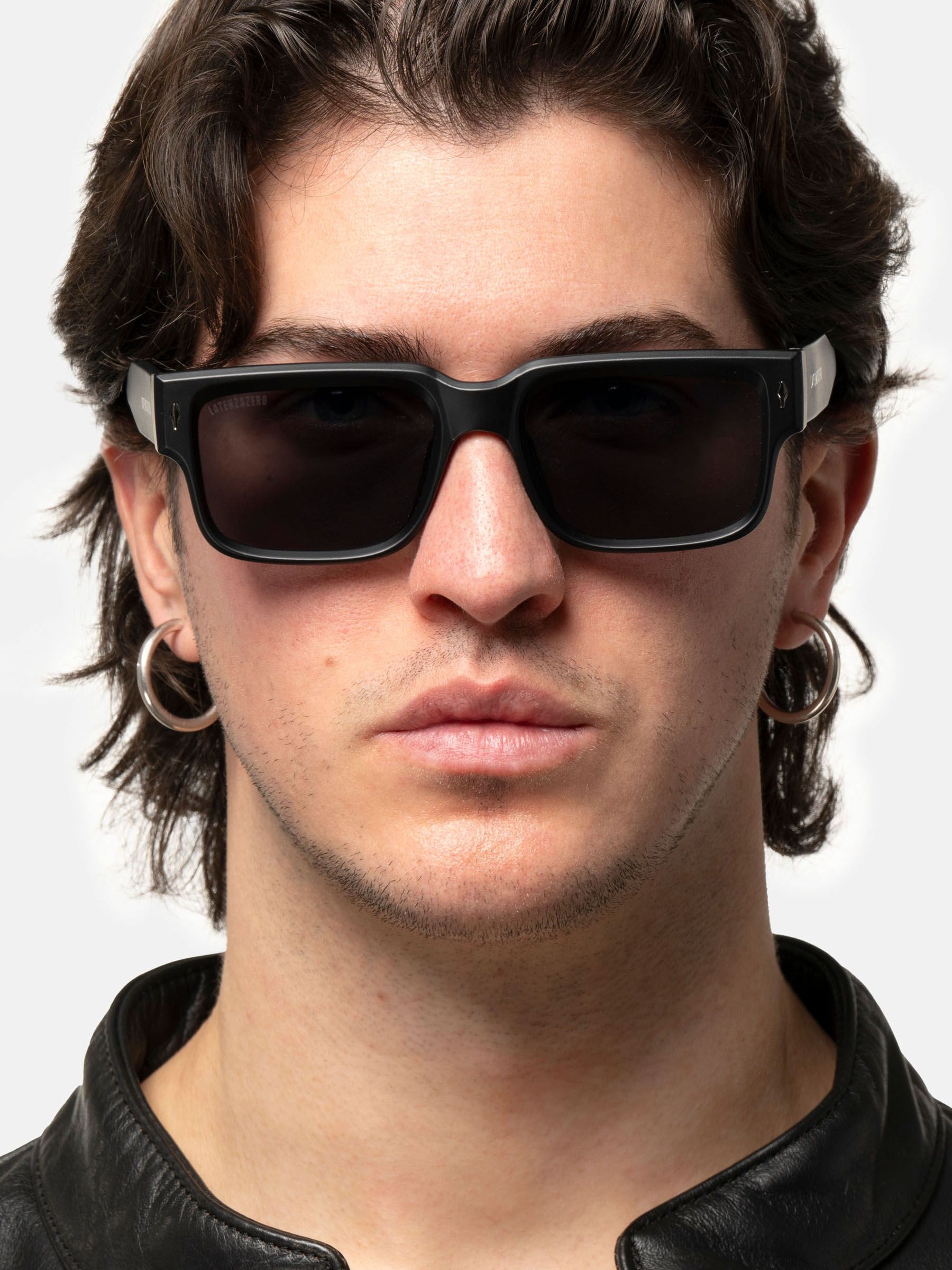 Uomo con occhiali da sole neri. Lenti rettangolari, logo sull'asta.