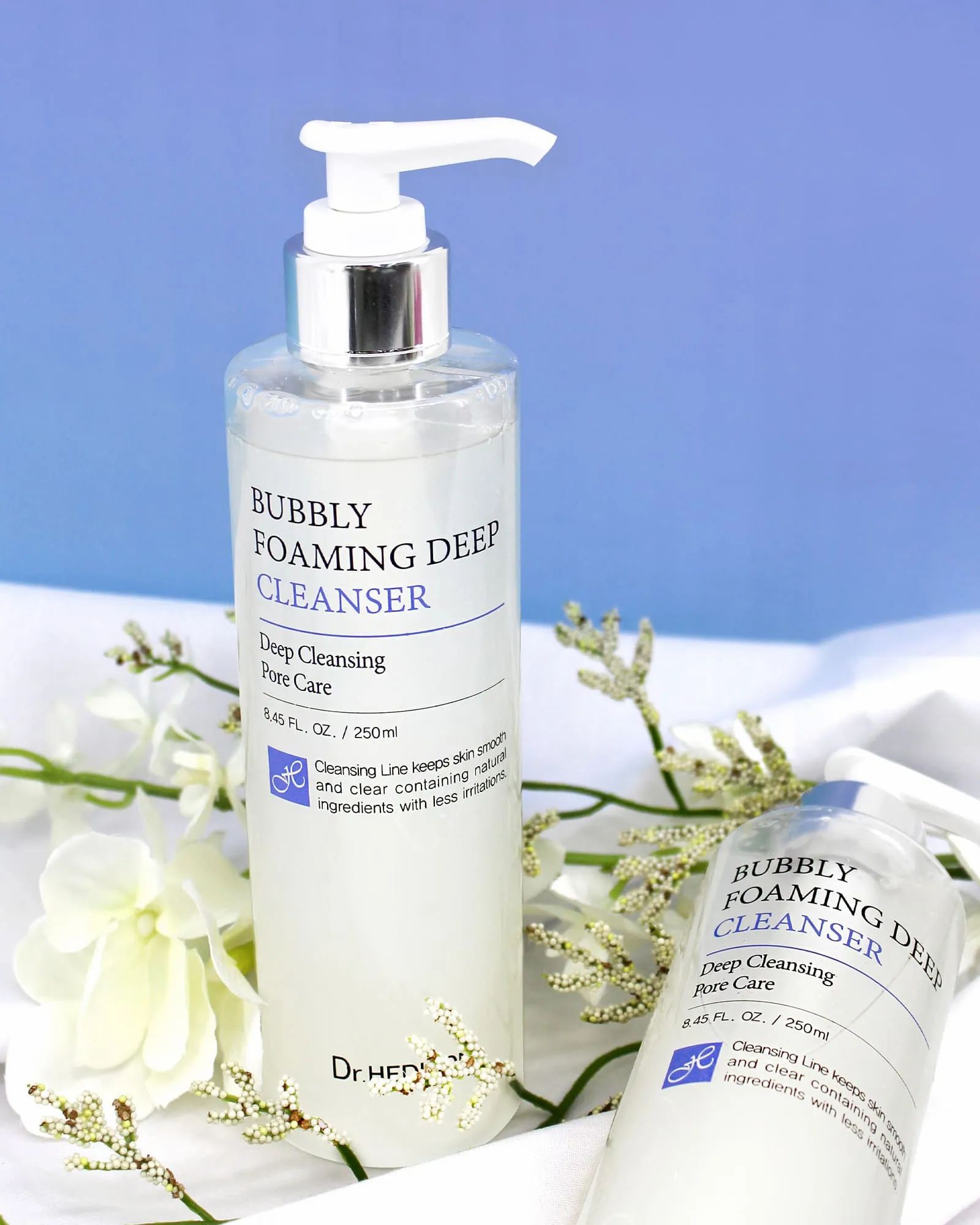 Due flaconi con dosatore. Scritta: Bubbly Foaming Deep Cleanser. Marchio: Dr. Hedison. Su tessuto bianco.