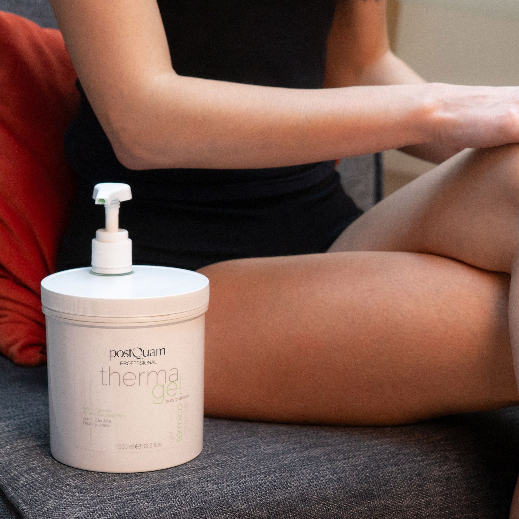 Donna seduta con contenitore bianco 'PostQuam therma gel'. Pompa sul contenitore. Indossa top nero.