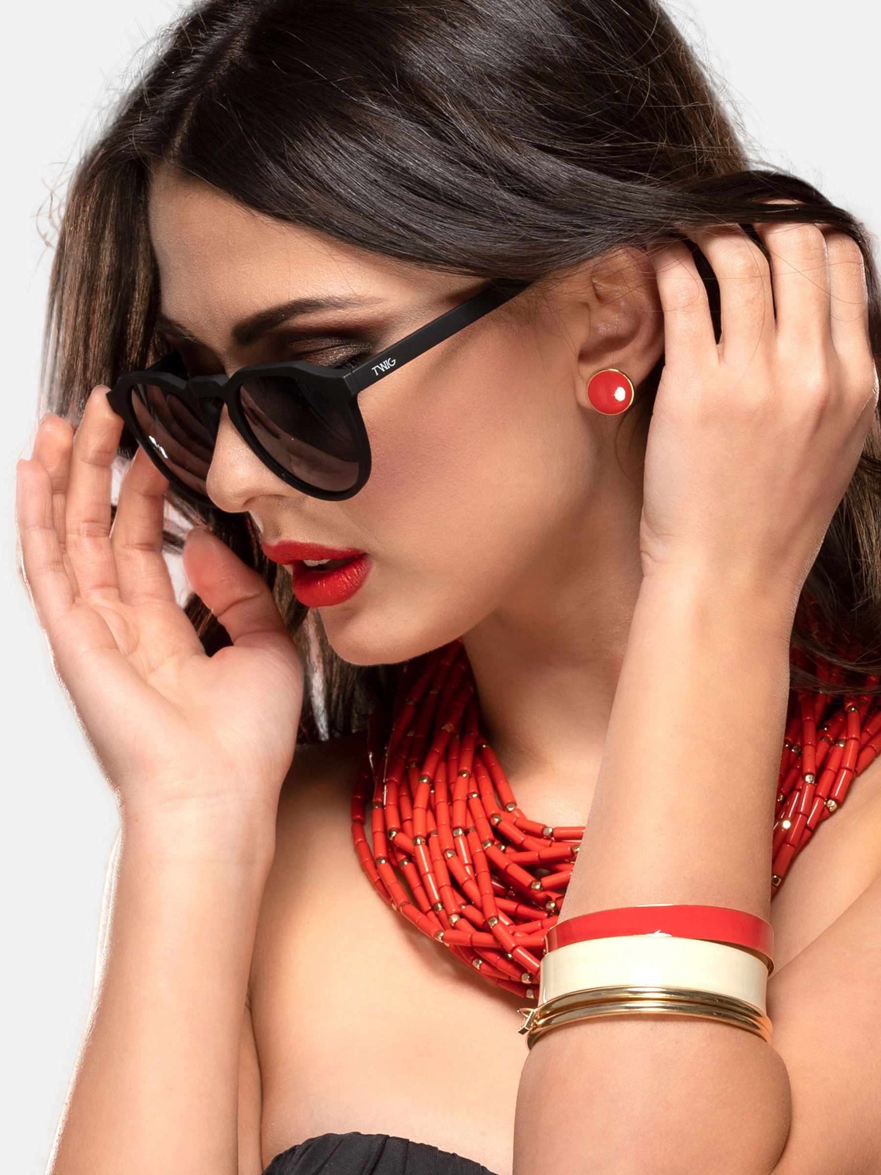 Donna con occhiali da sole neri. Labbra rosse, collana e bracciali. Occhiali con logo.