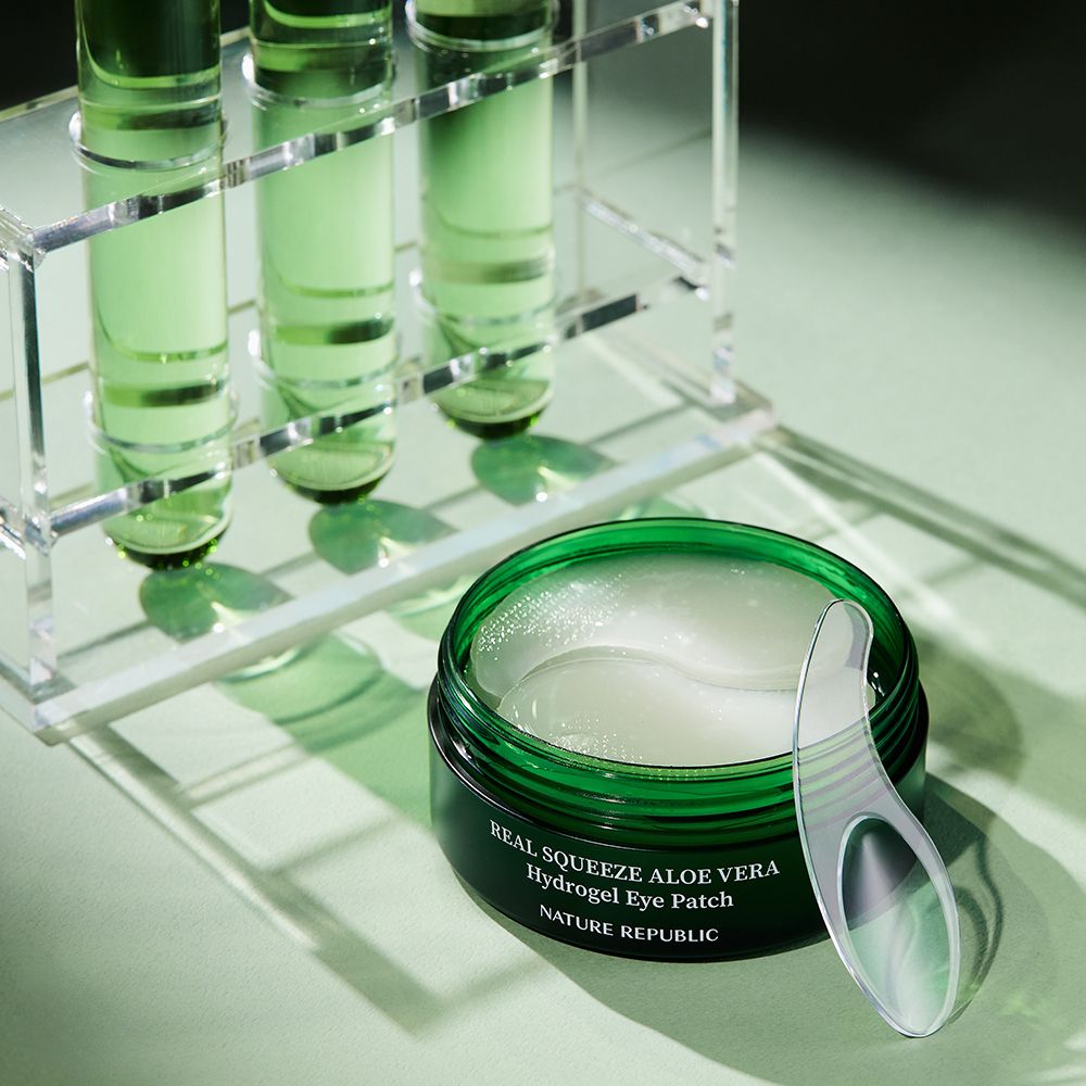 Barattolo verde con patch idrogel per occhi e spatola. Vetreria da laboratorio sullo sfondo.