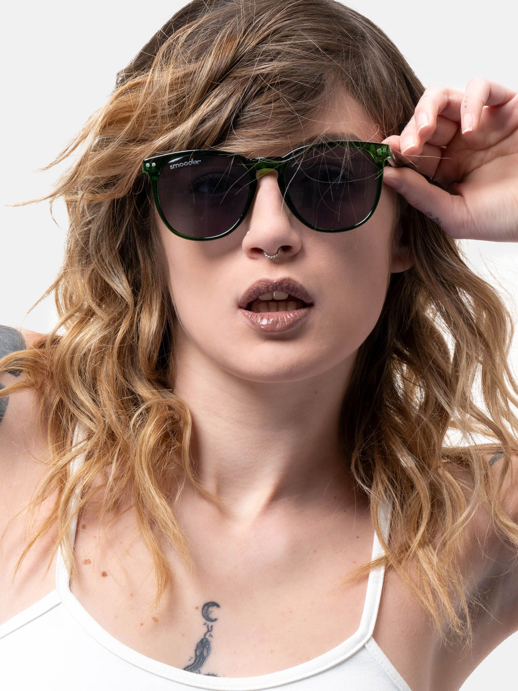 Persona indossa occhiali da sole verdi. Forma rotonda, lenti scure. Marchio Smooder sulla stanghetta. Donna tiene gli occhiali.