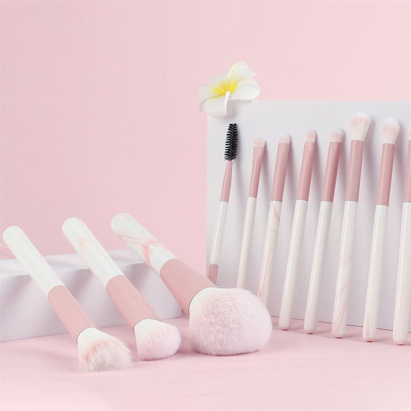 Set di pennelli per trucco. Pennelli con manici rosa e bianchi. Varie forme e dimensioni. Posizionati su una superficie rosa. Alcuni pennelli sono in piedi.