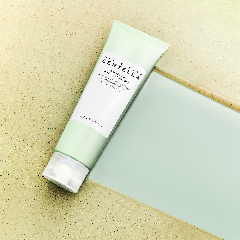 Tubo verde con etichetta bianca. Testo: MADAGASCAR CENTELLA, Tea-Trica Mild Peeling Gel. Su una superficie.