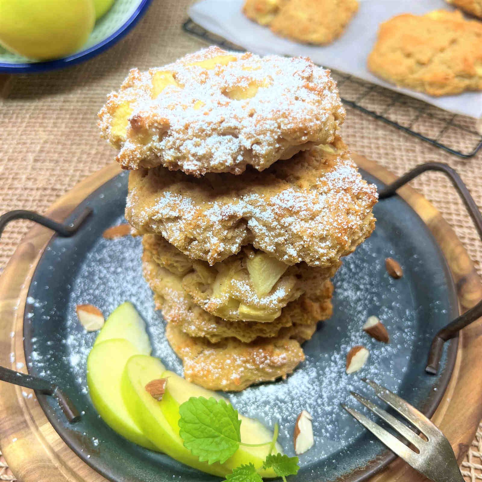 Biscotti impilati, spolverati di zucchero a velo, con pezzi di mela. Decorato su un vassoio con mandorle e fette di mela.