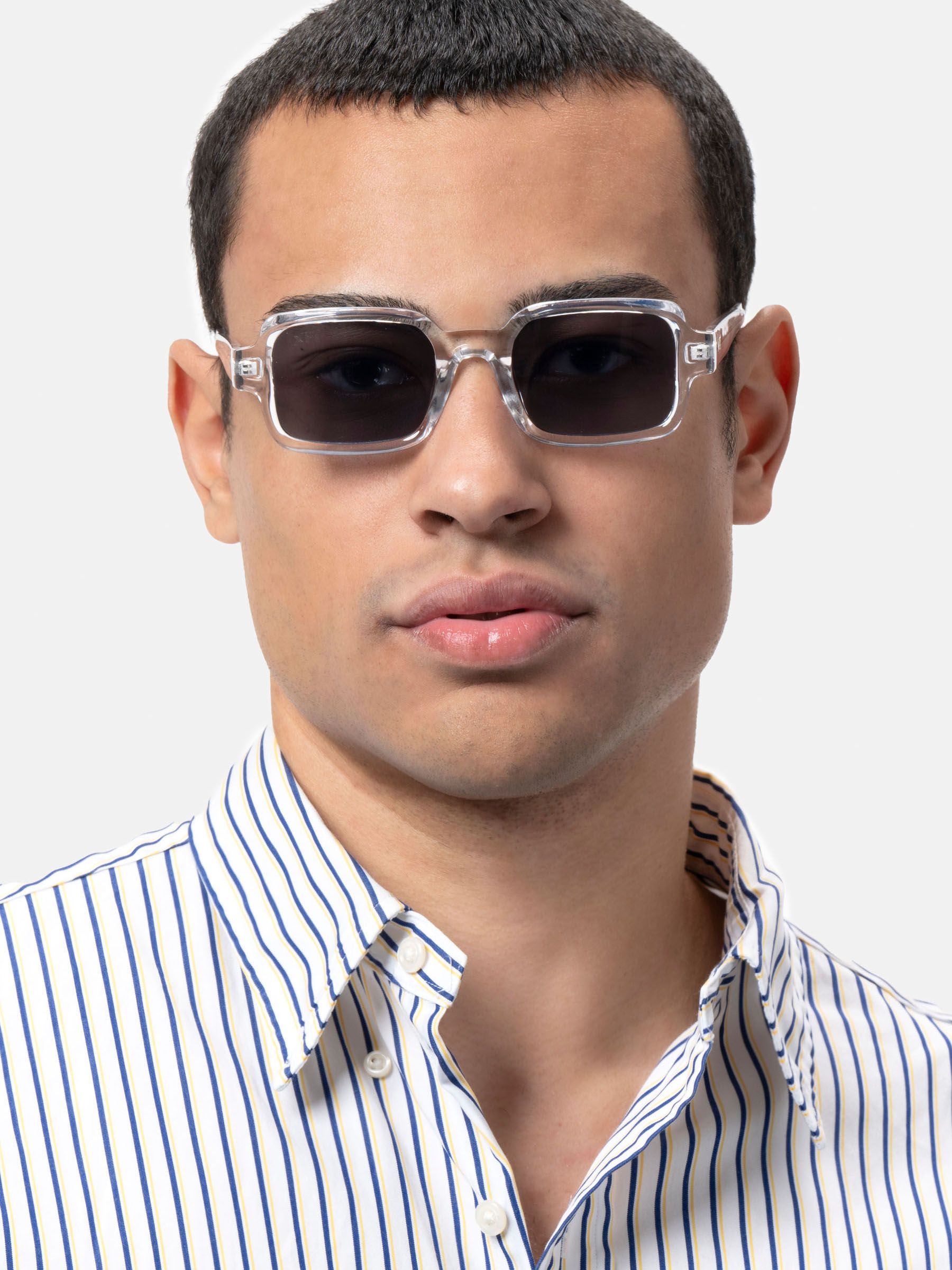 Uomo con occhiali da sole rettangolari con montatura trasparente e lenti scure. Camicia a righe. Primo piano.