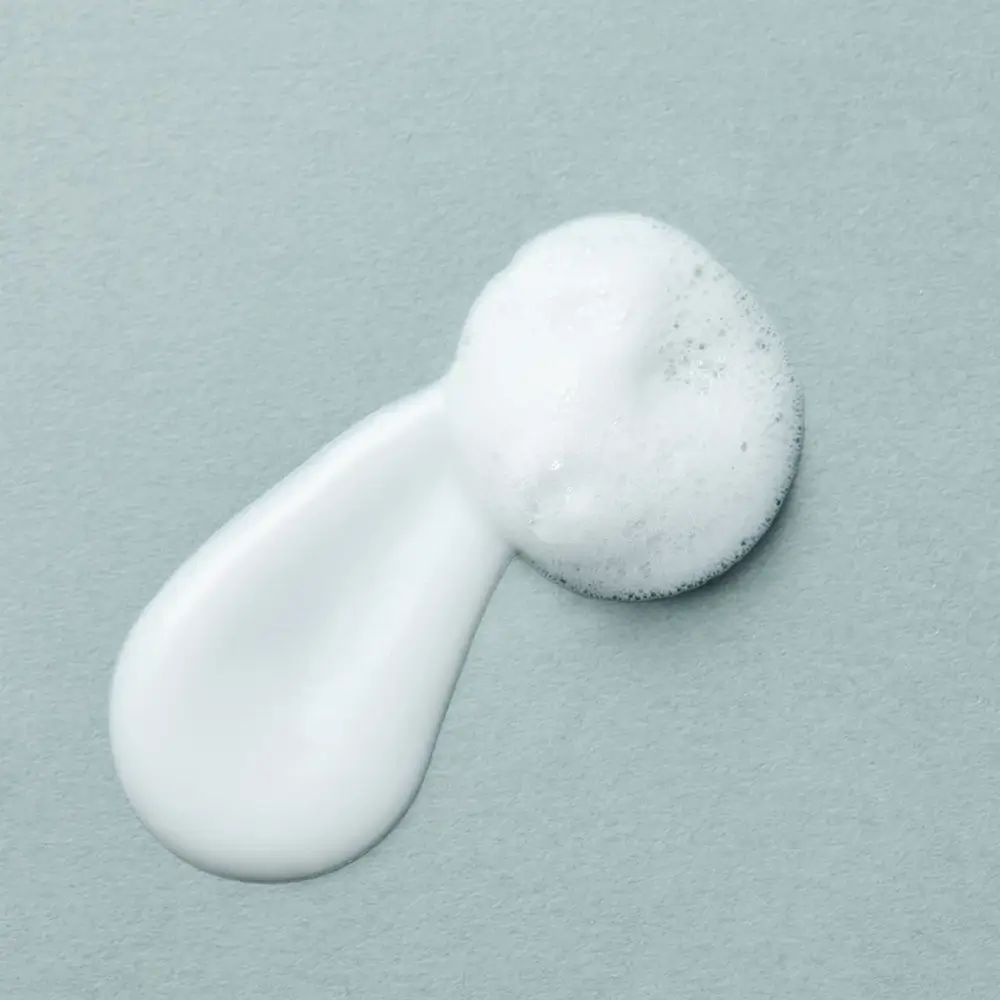 Goccia di crema e schiuma su sfondo grigio. Consistenza visibile.