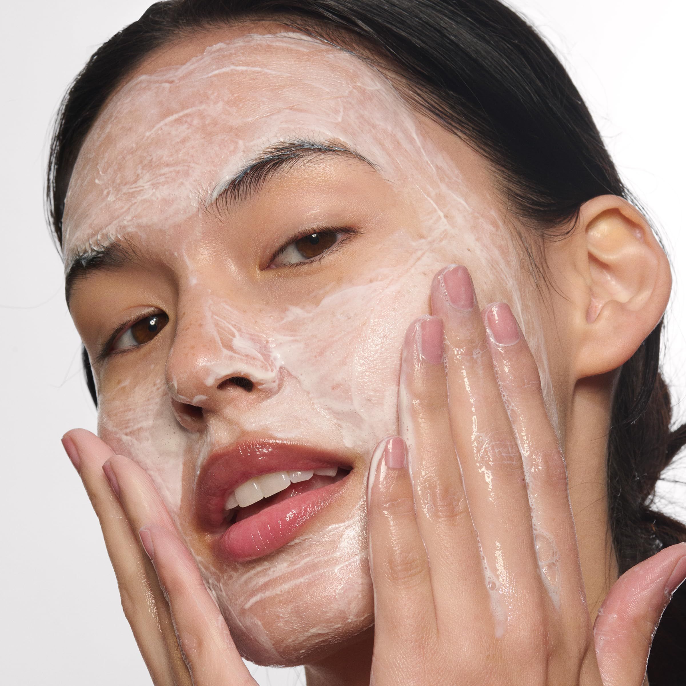 Viso di donna con schiuma sulla pelle. Si tocca il viso con le mani.