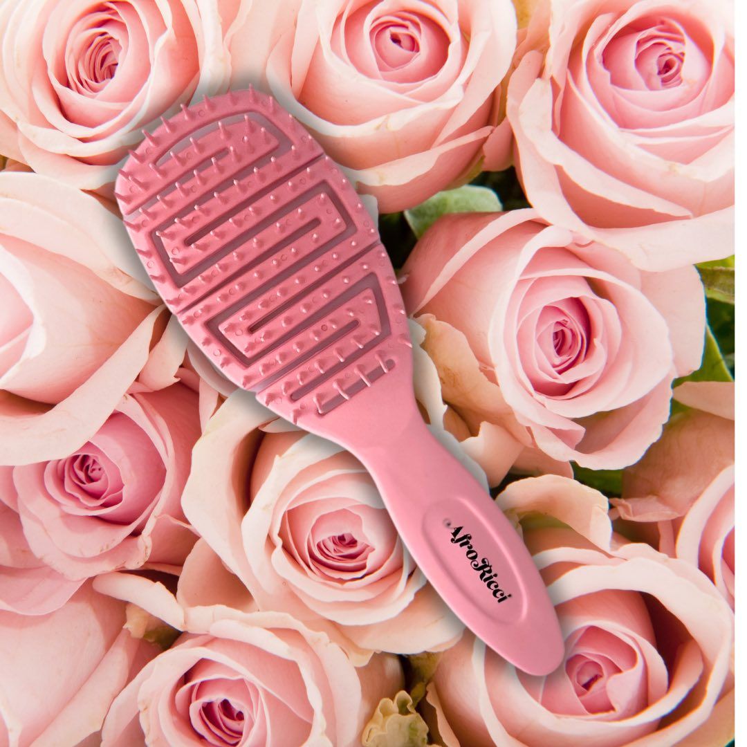 Spazzola rosa con manico. La testa della spazzola ha una struttura a zig-zag. Sfondo: rose.