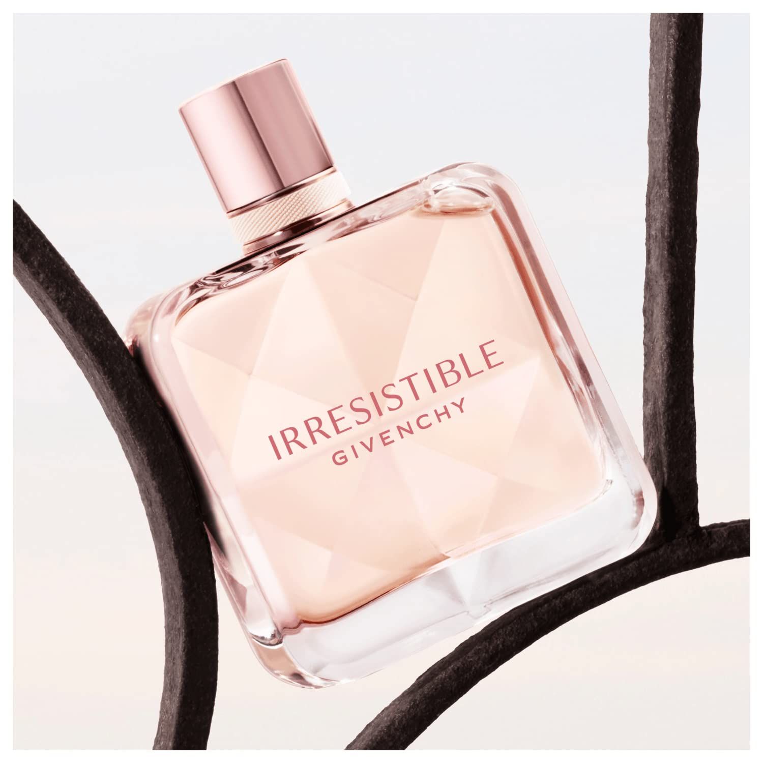 Flacone quadrato, contenuto rosa, davanti a una griglia metallica. Scritta: Irresistible Givenchy. Tappo rosa.