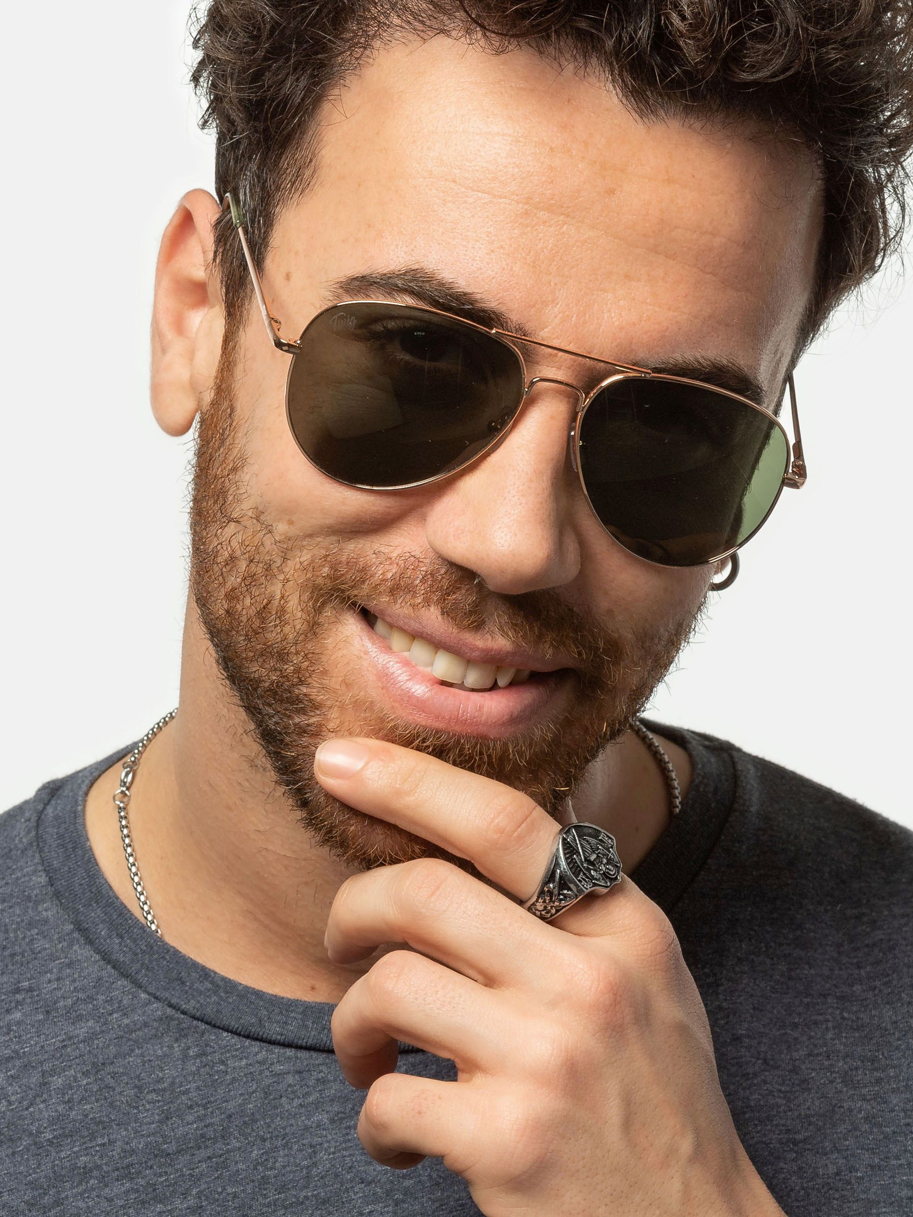Uomo con occhiali da sole dorati e lenti verdi. Visibili barba, anello e collana.