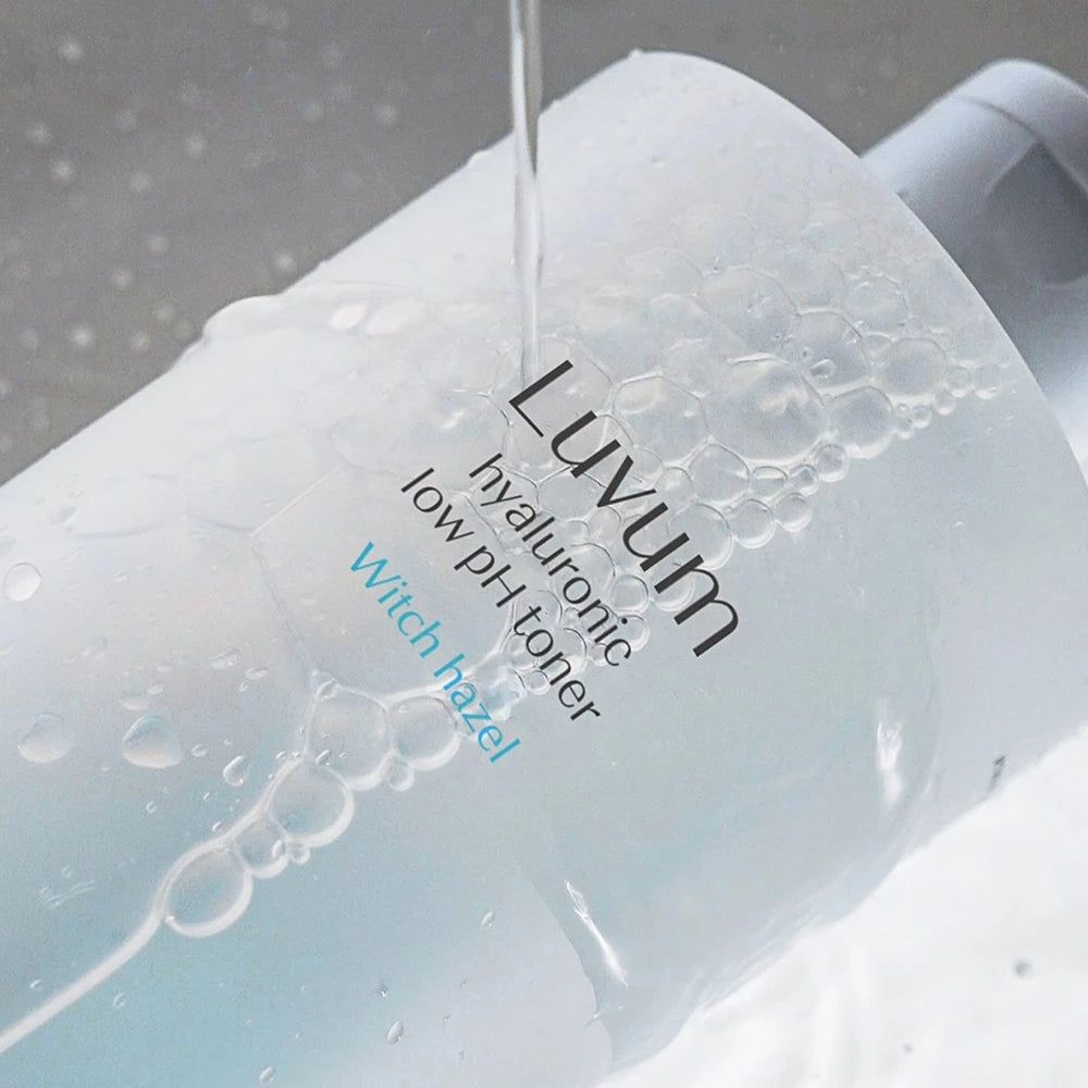 Liquido trasparente che scorre su una bottiglia. La bottiglia reca la scritta "Luvum hyaluronic low pH toner Witch hazel".
